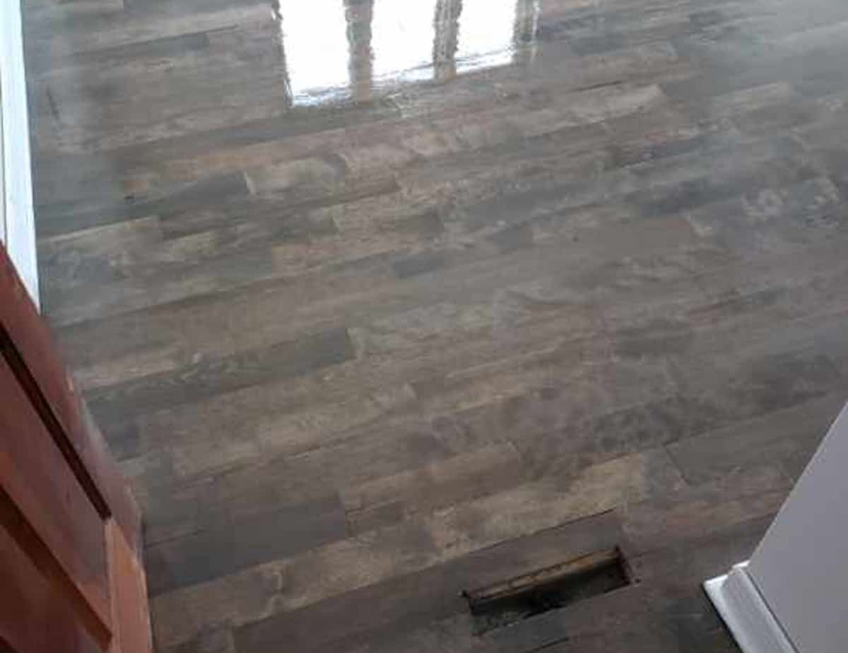 Plancher de bois franc foncé et teinté avec finition brillante, grille d'aération visible.