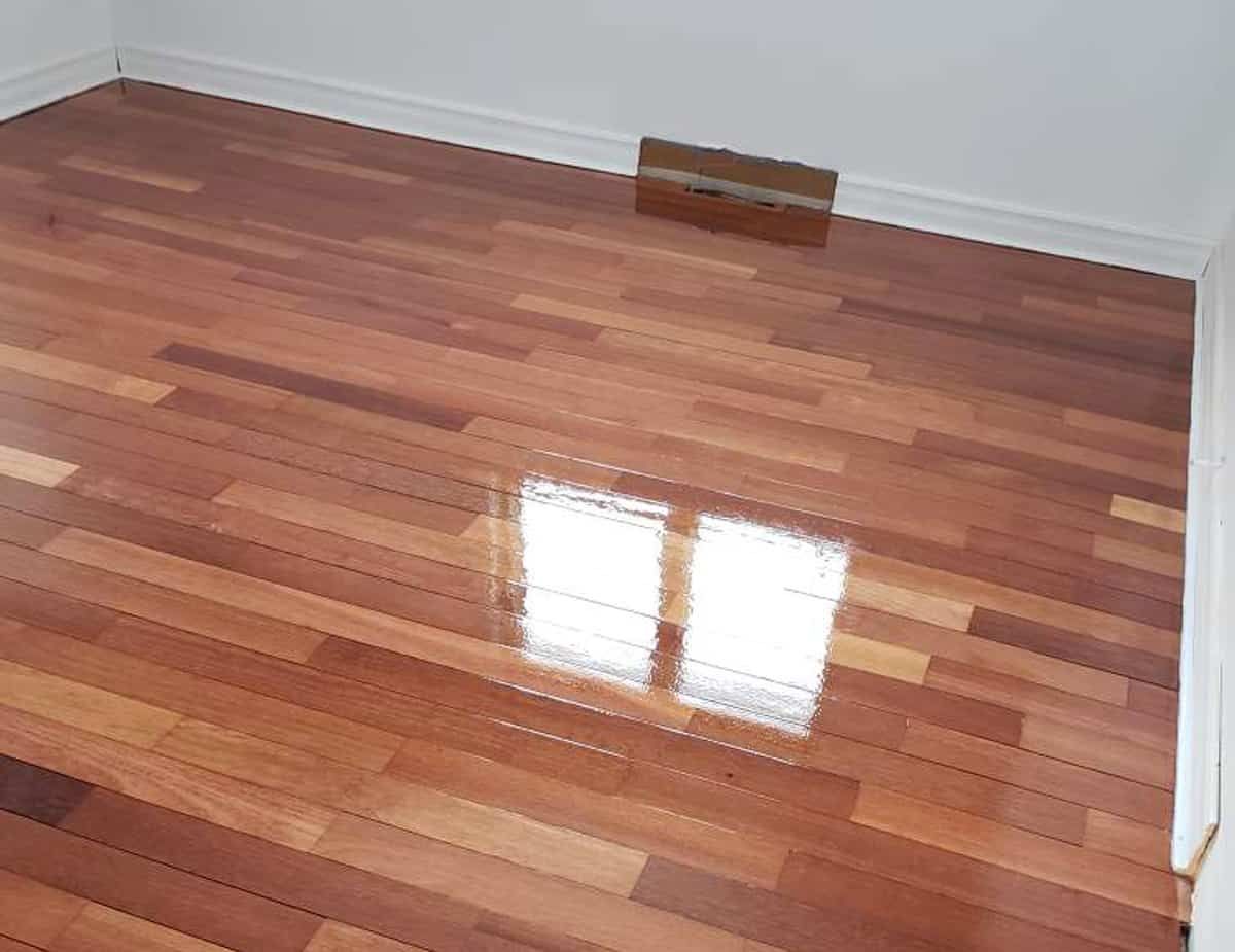 Un plancher en bois brillant et poli reflétant la lumière du soleil à travers une fenêtre, dans une pièce vide.