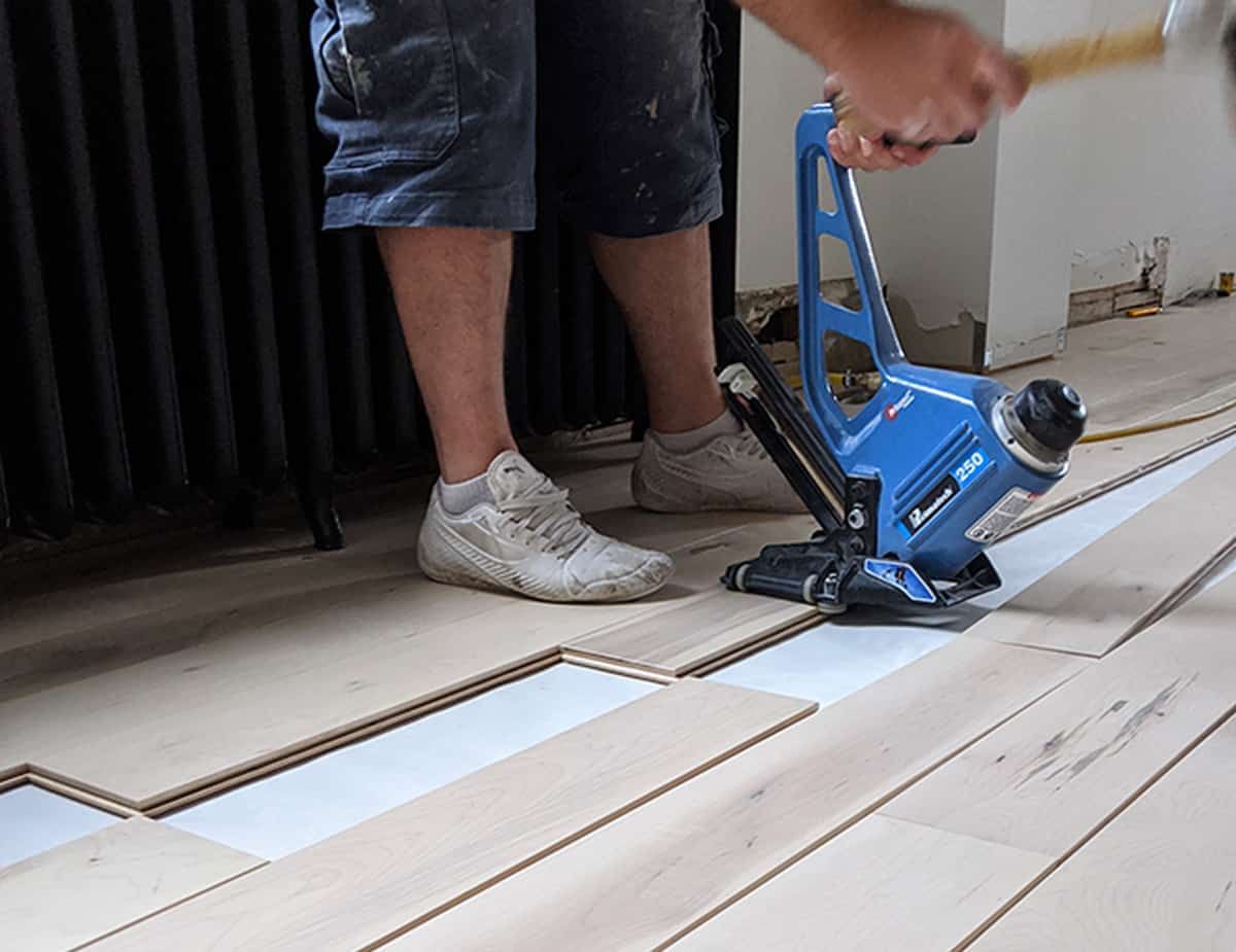 Personne utilisant une cloueuse à plancher bleue pour installer un plancher en bois, à l'intérieur.