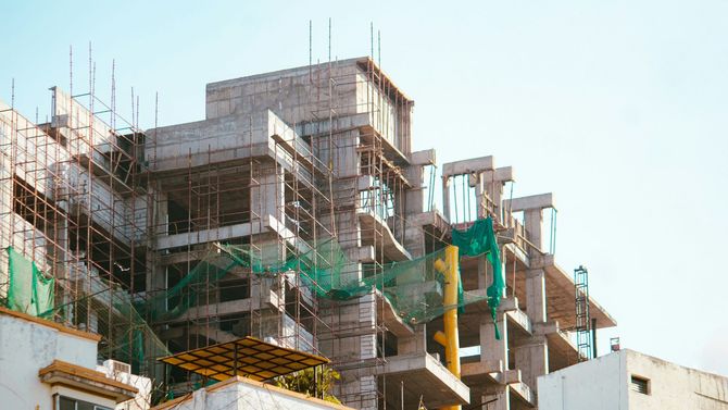 Scaffolding on a multi-story building under construction, with green safety netting and exposed concrete.