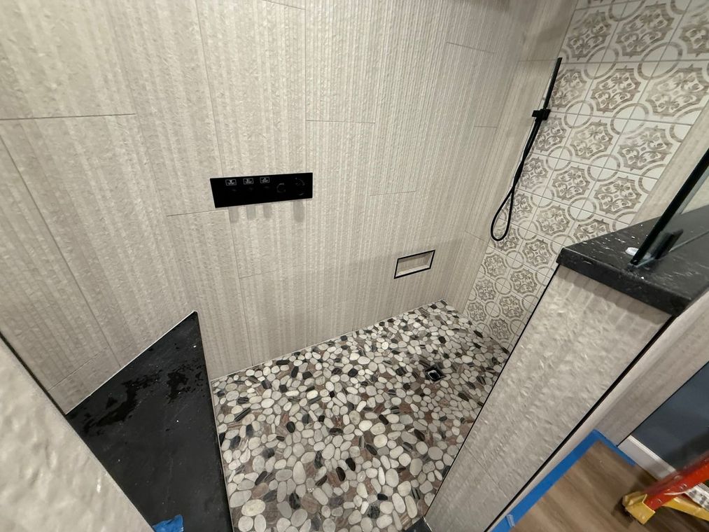 Small tiled shower stall with patterned floor, wall controls, and a shower hose.