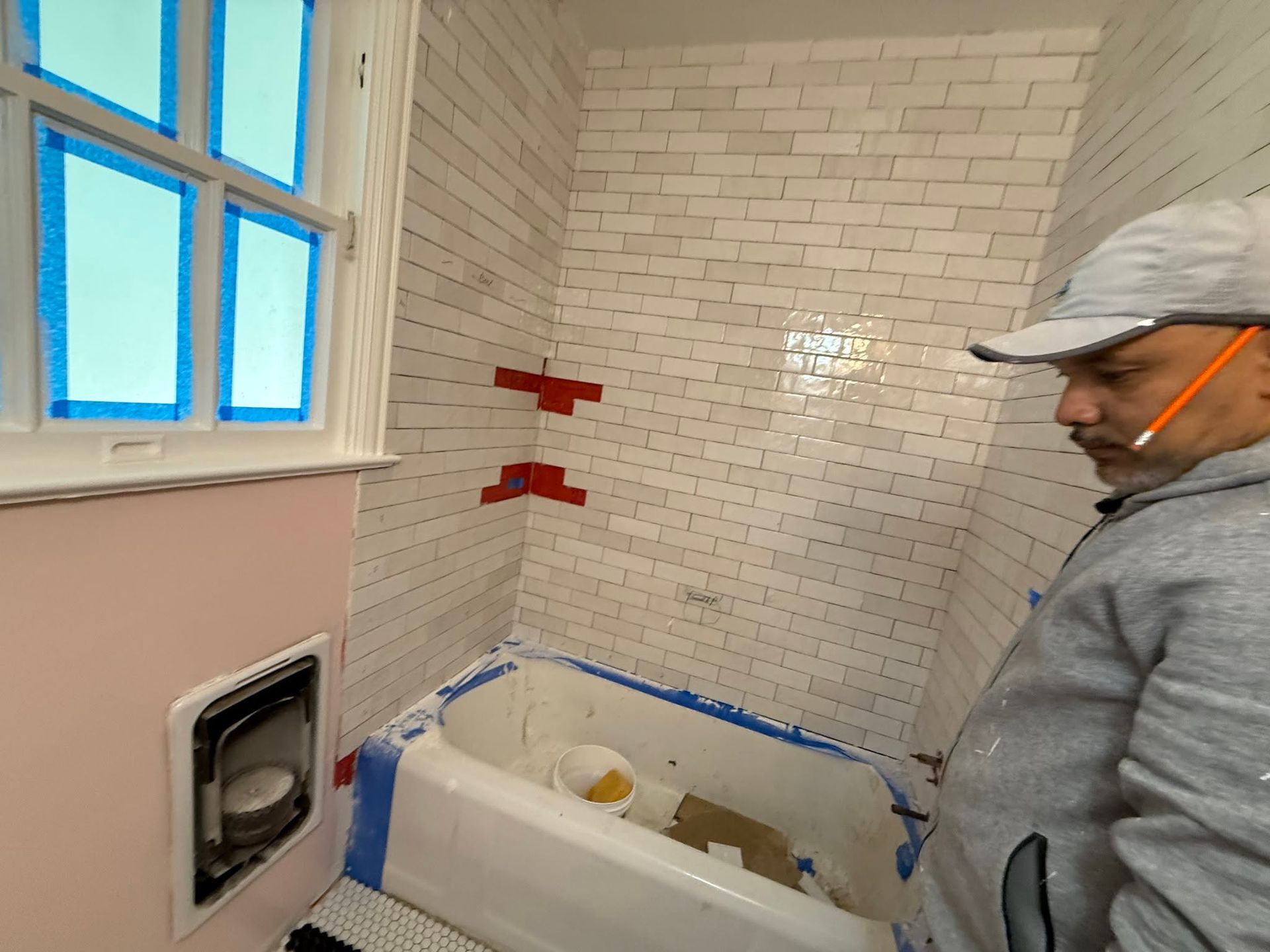 Man in gray hoodie and cap standing in a tiled bathroom with a bathtub under renovation