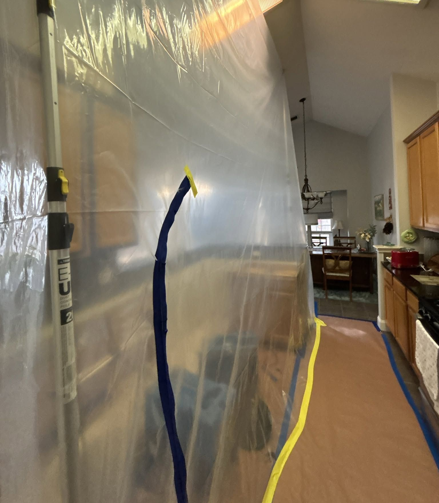 Hallway with a large translucent panel and blue/yellow taped edges beside a kitchen area