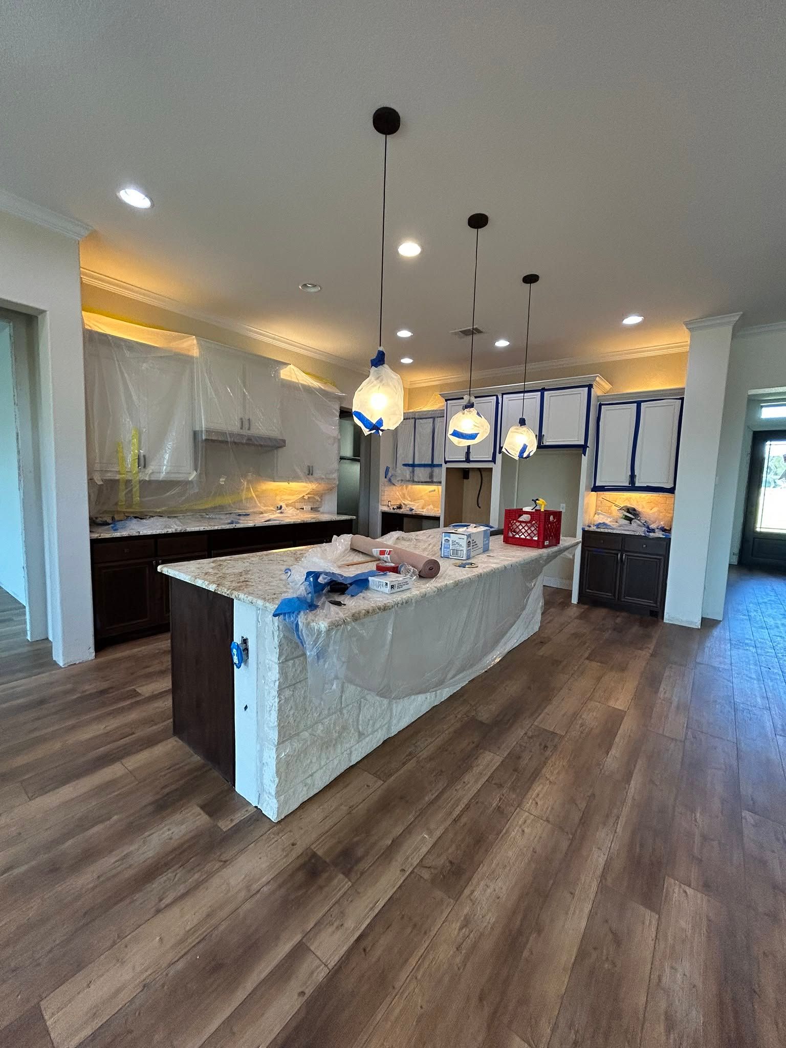 Open-plan kitchen with large island, pendant lights, dark wood floors, and white cabinets