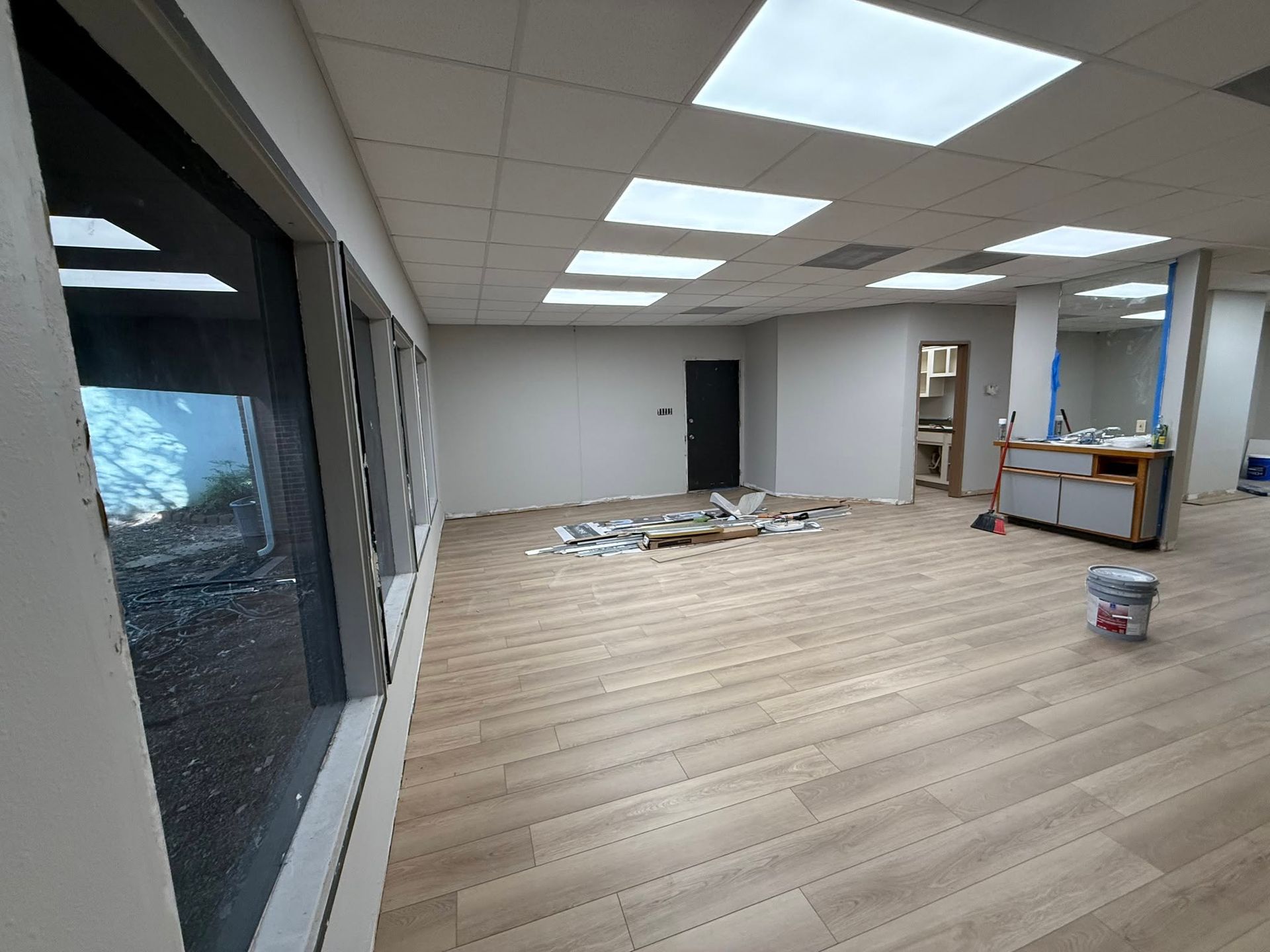 Empty office space with light wood flooring, ceiling lights, and a counter area under renovation