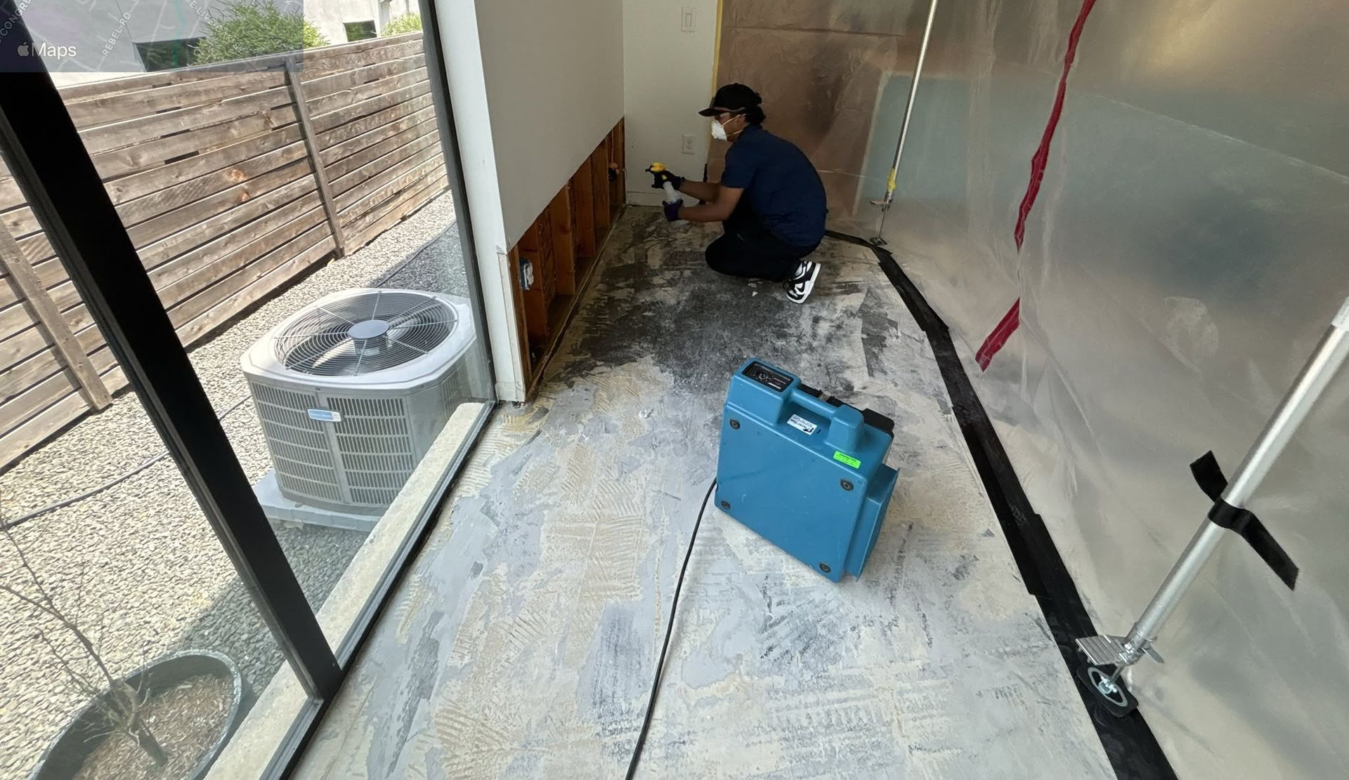 Worker crouches by a wall in a partially finished room with tools and debris on the floor.