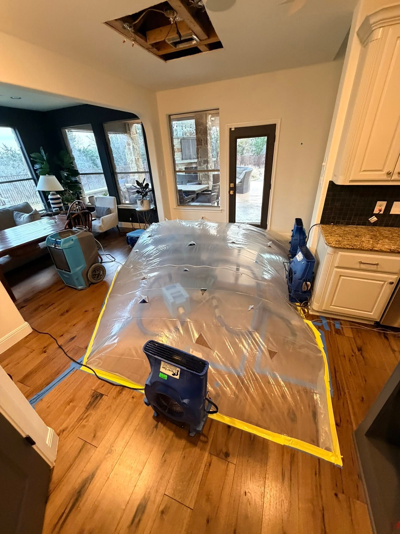 Living room with a clear inflatable tent on a hardwood floor near a kitchen area.