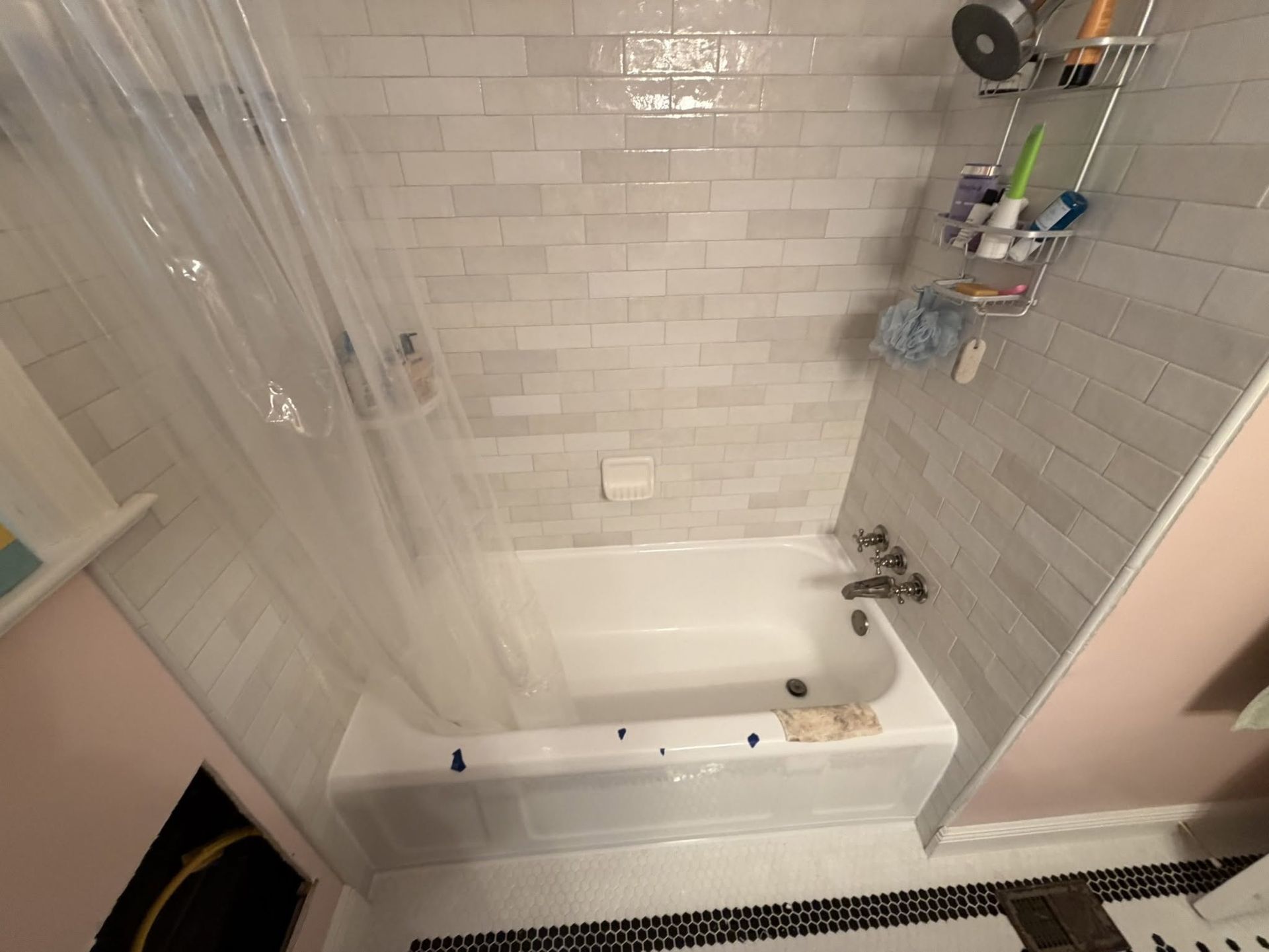 Small bathroom with a white bathtub, tiled walls, shower curtain, and shelf of toiletries.
