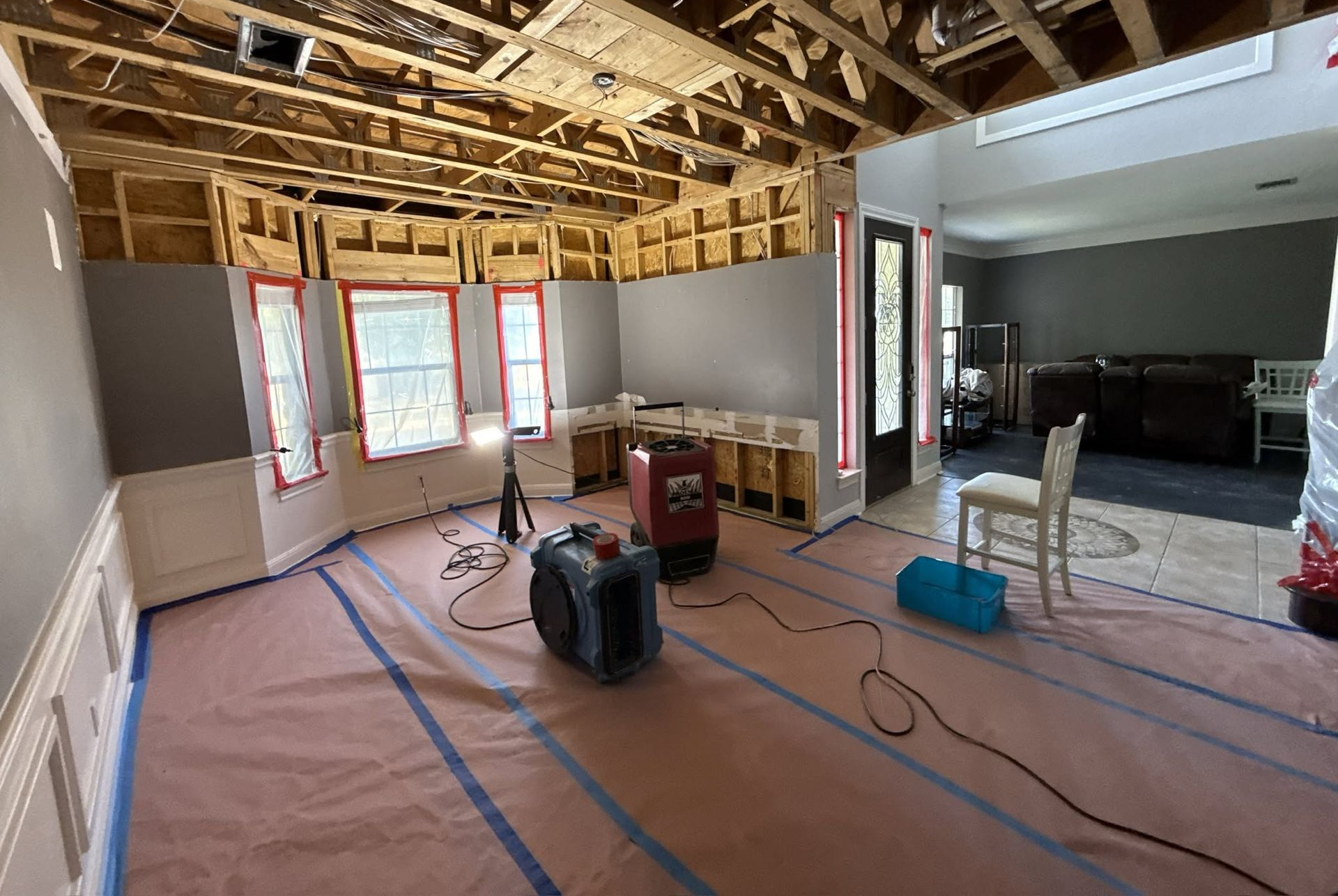 Partially renovated room with exposed ceiling joists, covered floor, windows, and construction tools