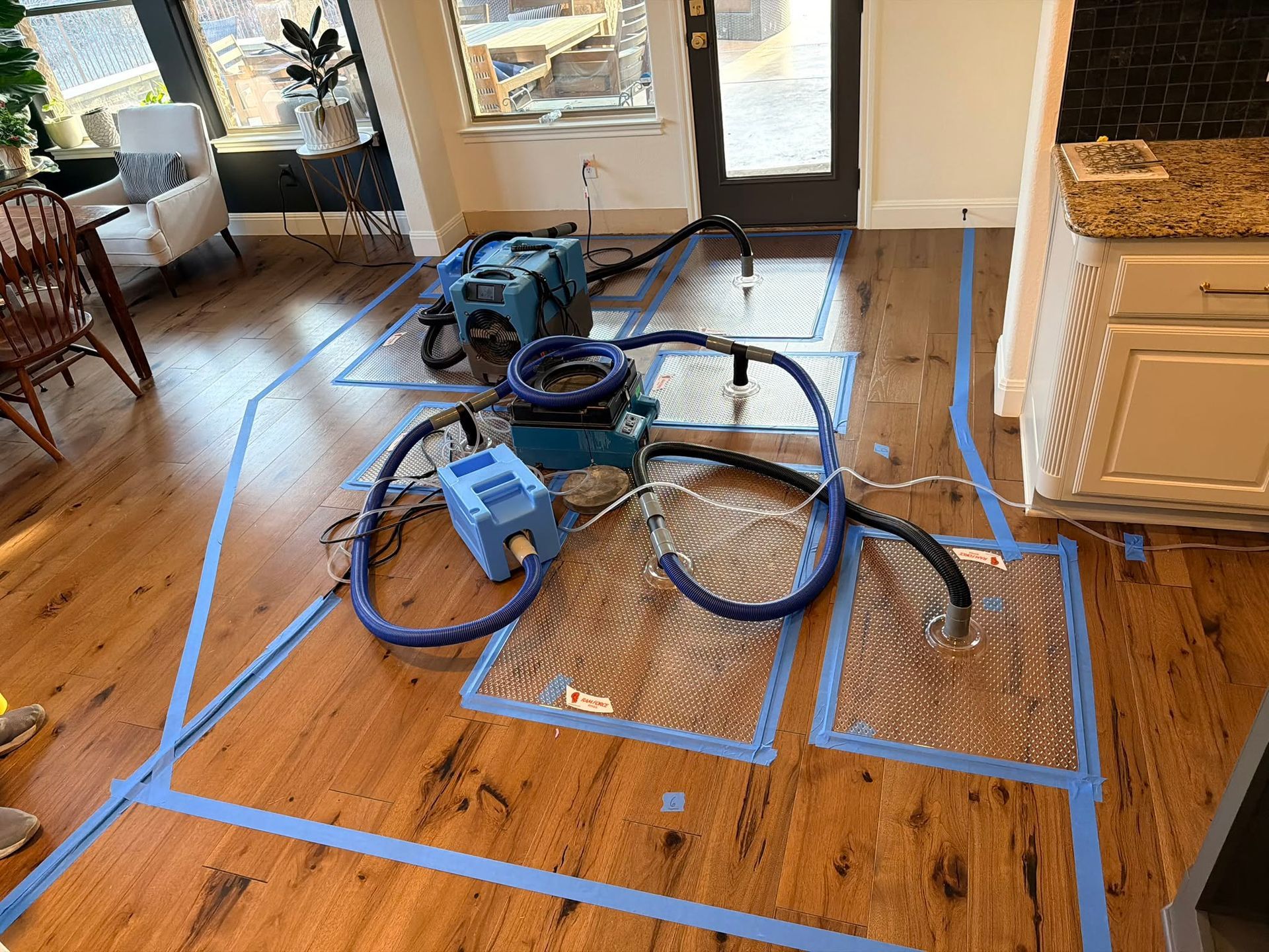 Blue tape marks a furniture layout on a hardwood floor, with a blue vacuum and hoses in the center.
