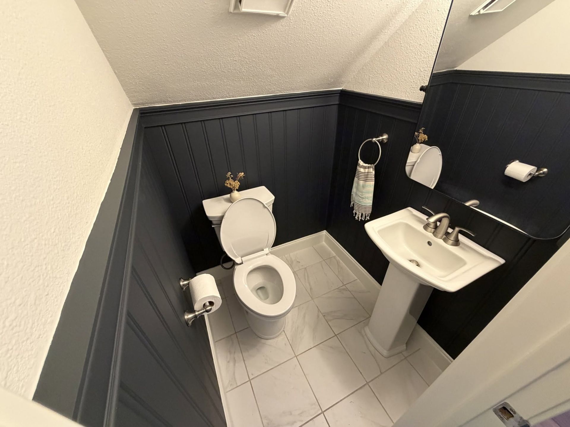 Small bathroom with toilet, sink, black wall panels, and white tile floor.