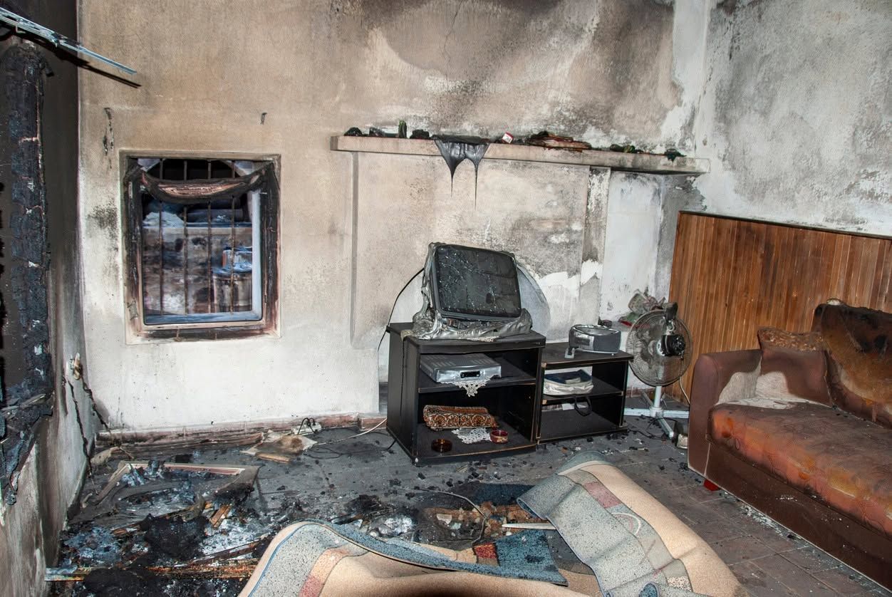 Fire-damaged living room with soot-covered walls, burned furniture, and debris on the floor