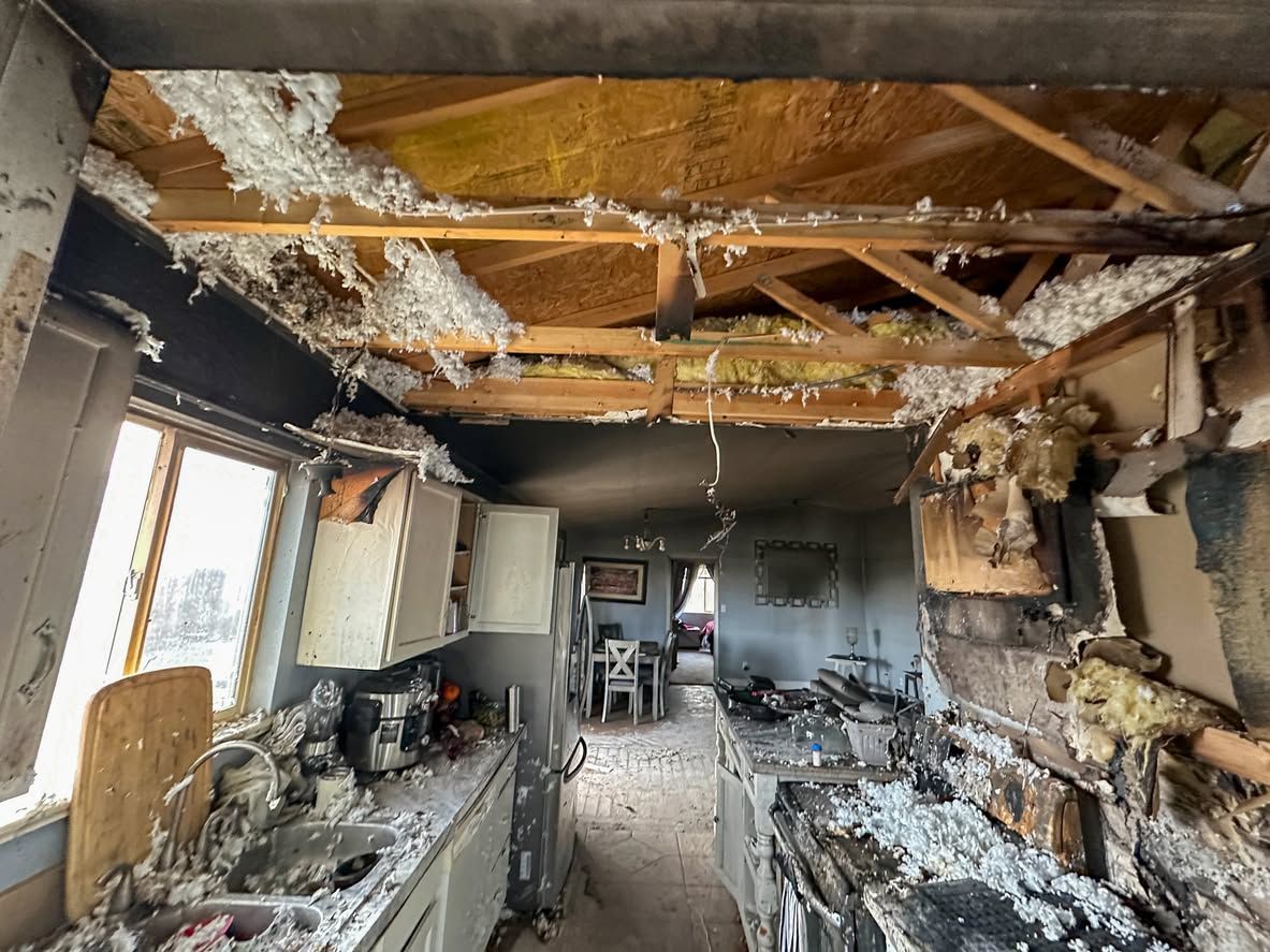 Fire-damaged kitchen with a collapsed ceiling, charred cabinets, and debris scattered across the room.