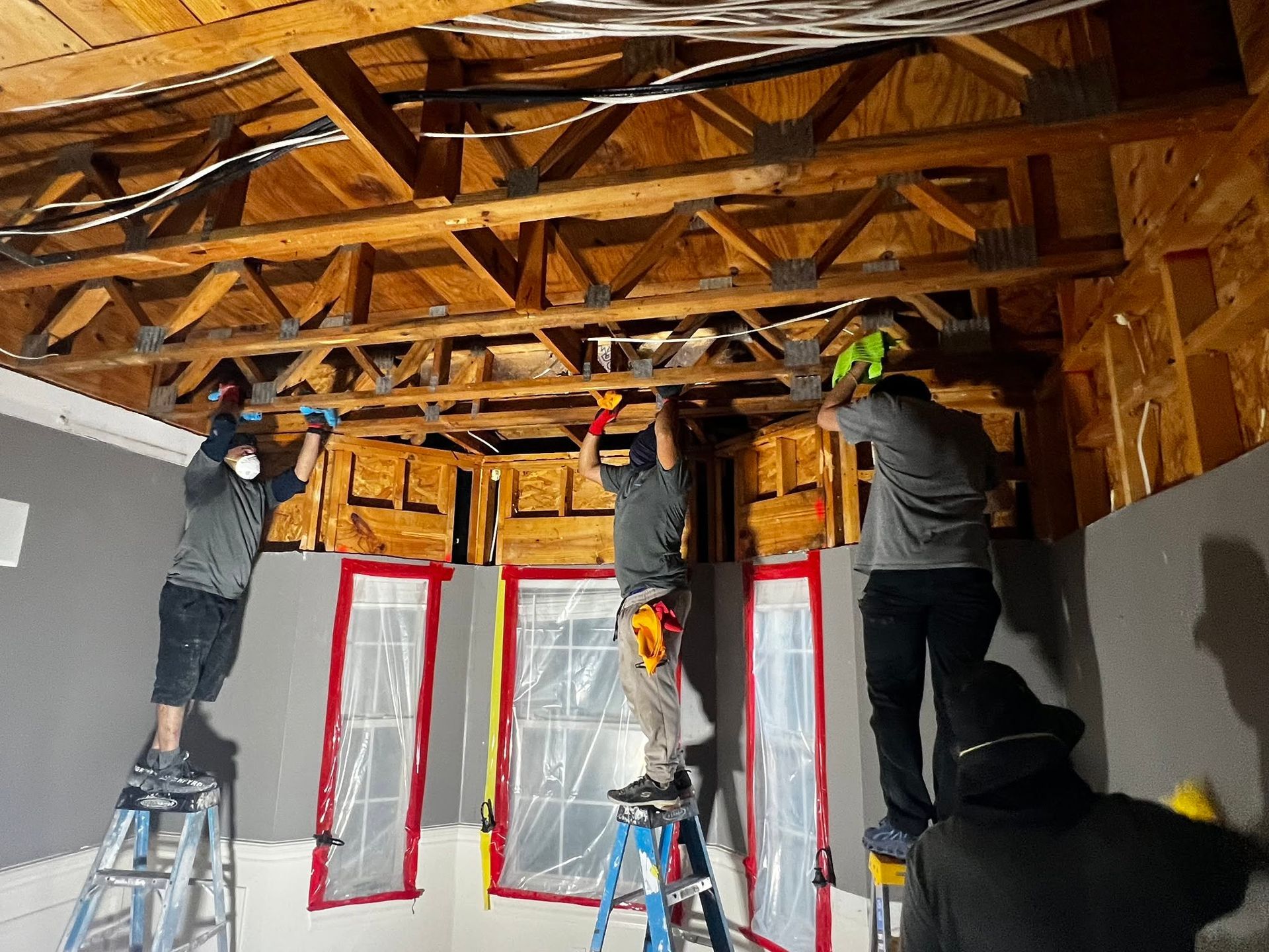 Workers installing insulation in a room with exposed wooden rafters and covered windows