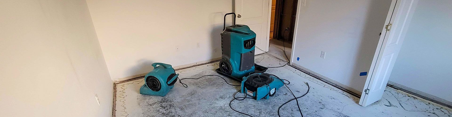Construction tools on a floor: a teal vacuum or drill, a teal machine, and cables in a white room.