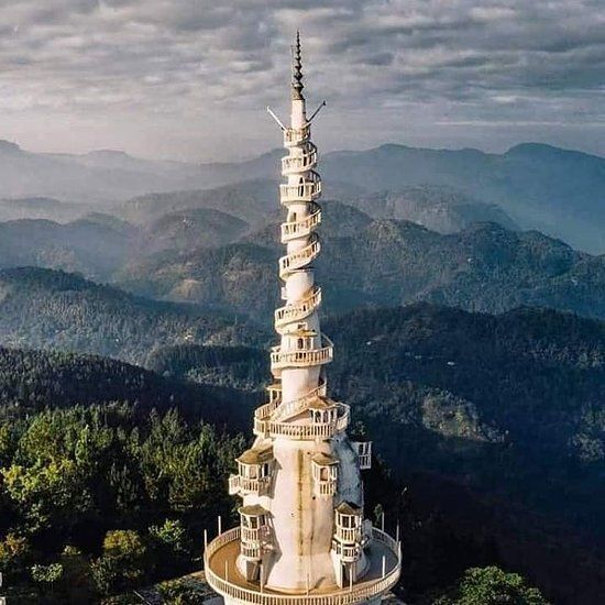 Tall spiral observation tower on a mountain ridge with forested hills in the background