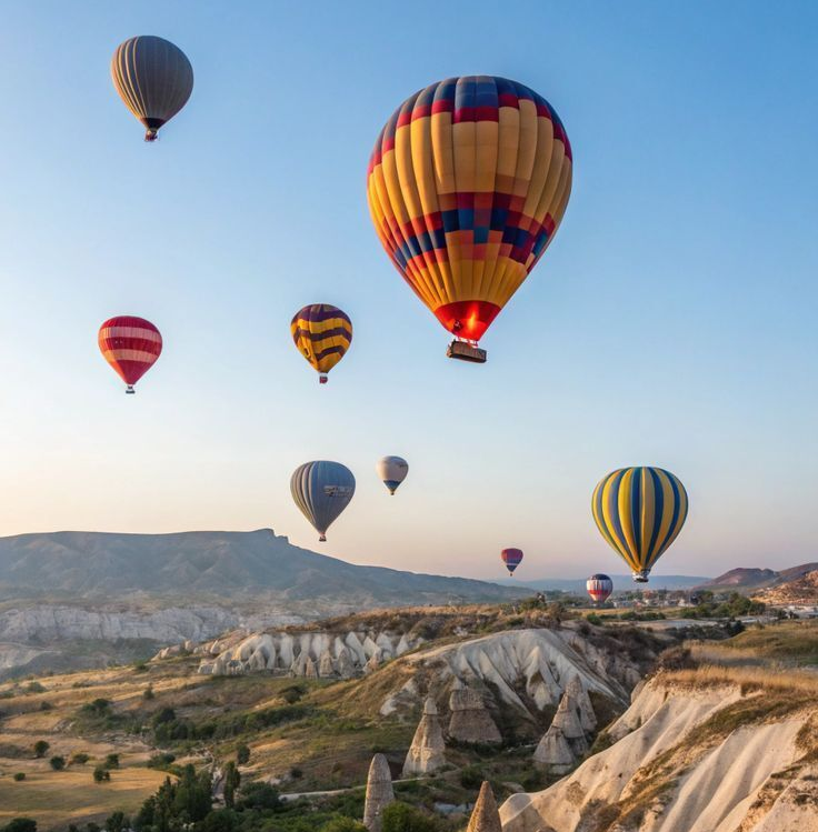 Hot air balloons of various colors float over a rocky valley at sunrise.