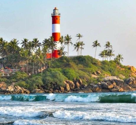 Red-and-white lighthouse on a tropical rocky shore with palm trees and ocean waves