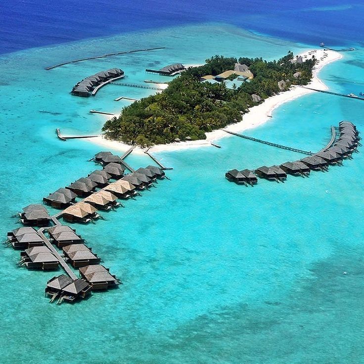 Aerial view of a tropical island resort with overwater bungalows in bright turquoise lagoon