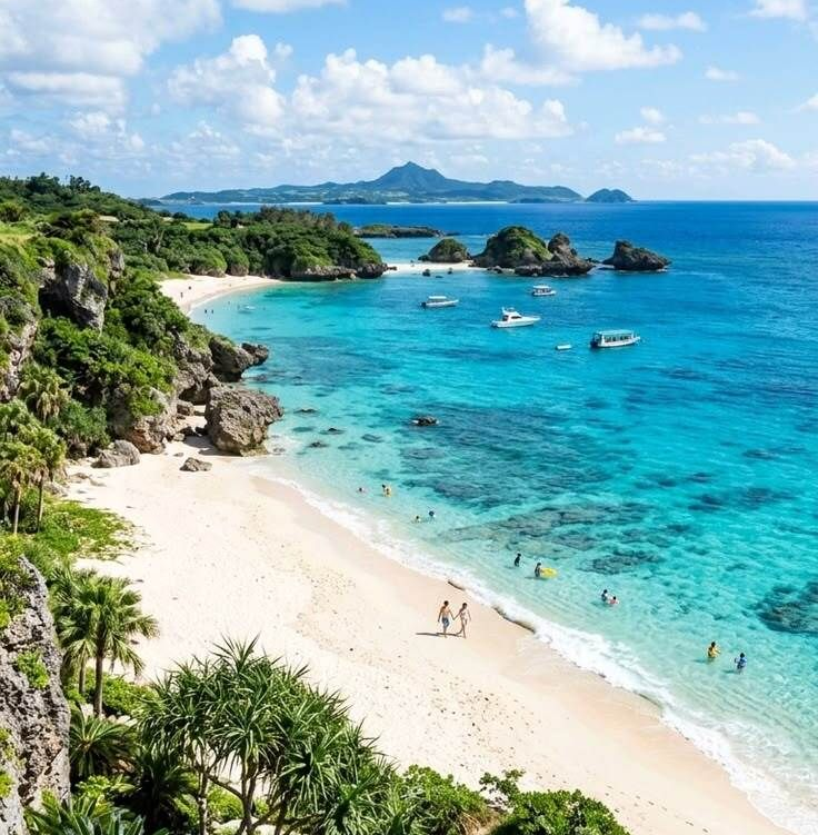 White sand tropical beach with turquoise water, boats, swimmers, and green cliffs under a bright sky