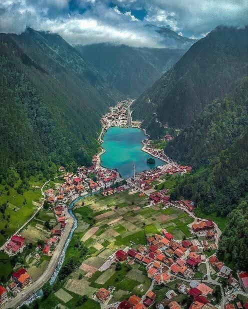 A turquoise mountain lake surrounded by steep green valleys and a village with red-roofed houses.