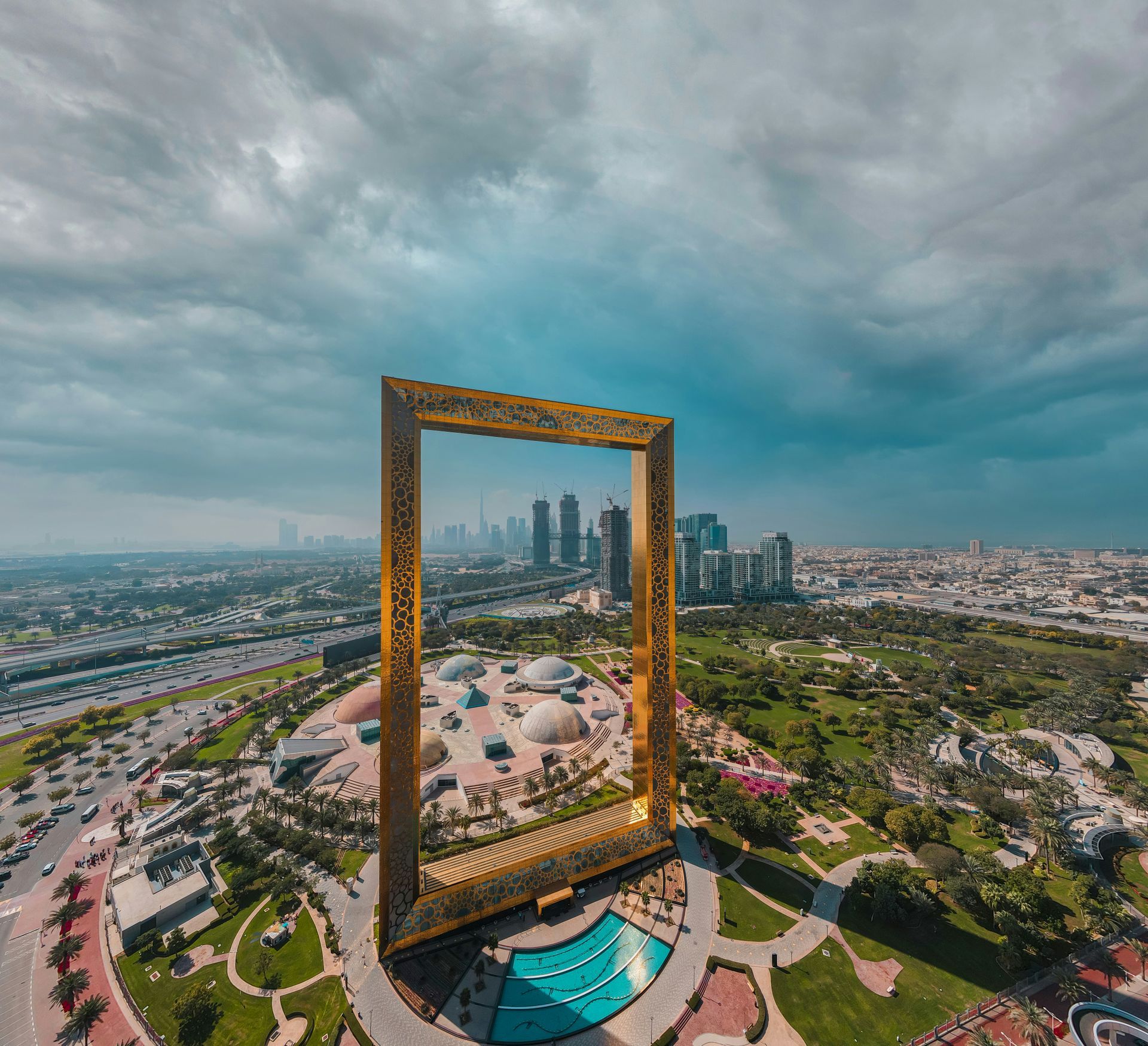 Gold frame monument overlooking a city skyline under dramatic cloudy skies