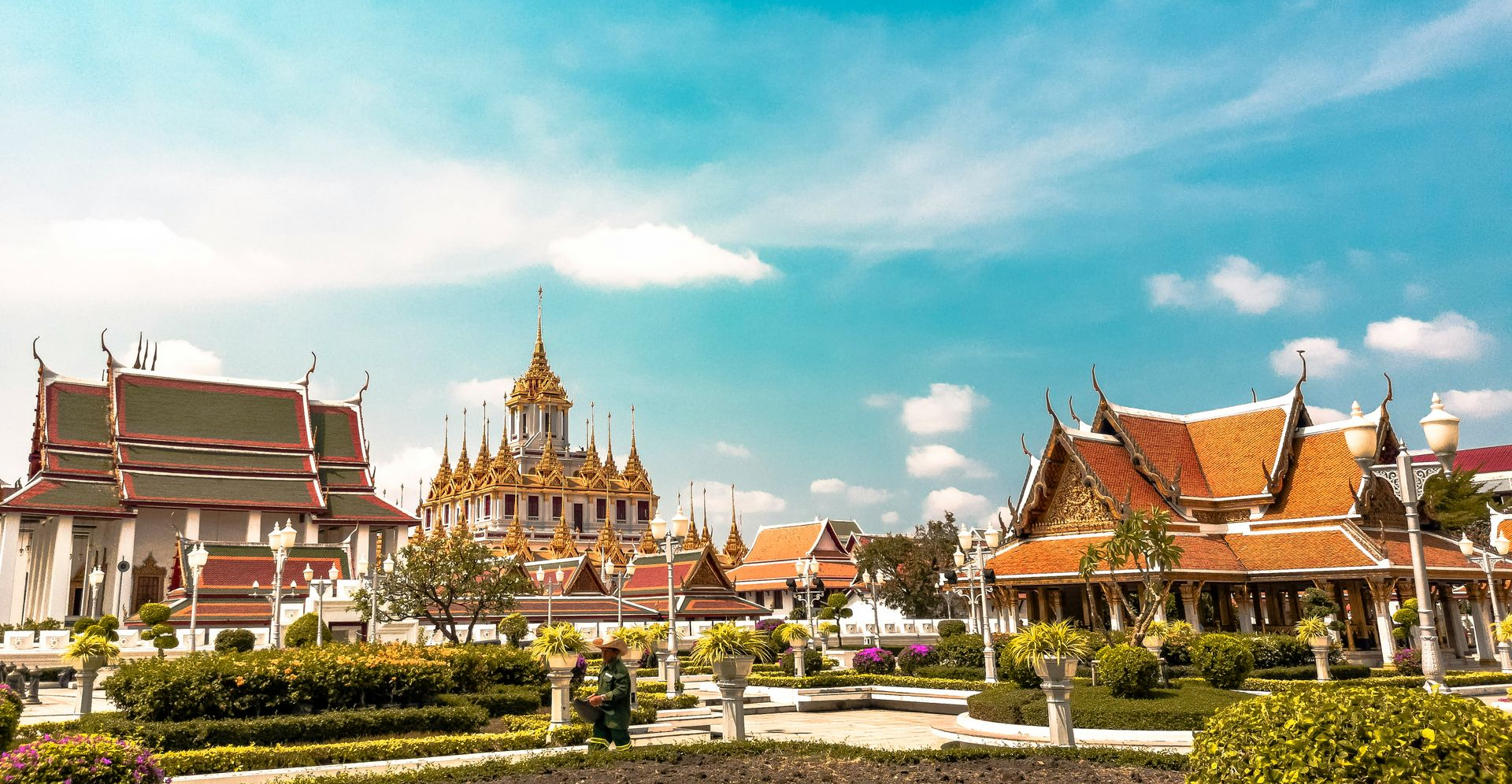 Temple complex with ornate golden spires and red-roofed buildings under a bright blue sky