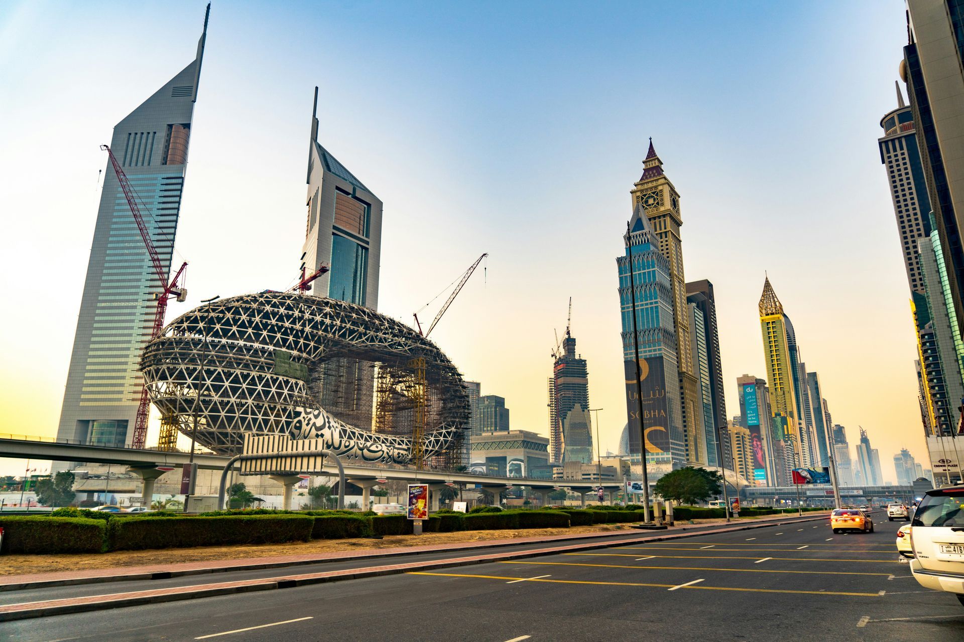 Dubai skyline at sunset with modern skyscrapers, a distinctive ring-shaped tower, and a busy road in the foreground