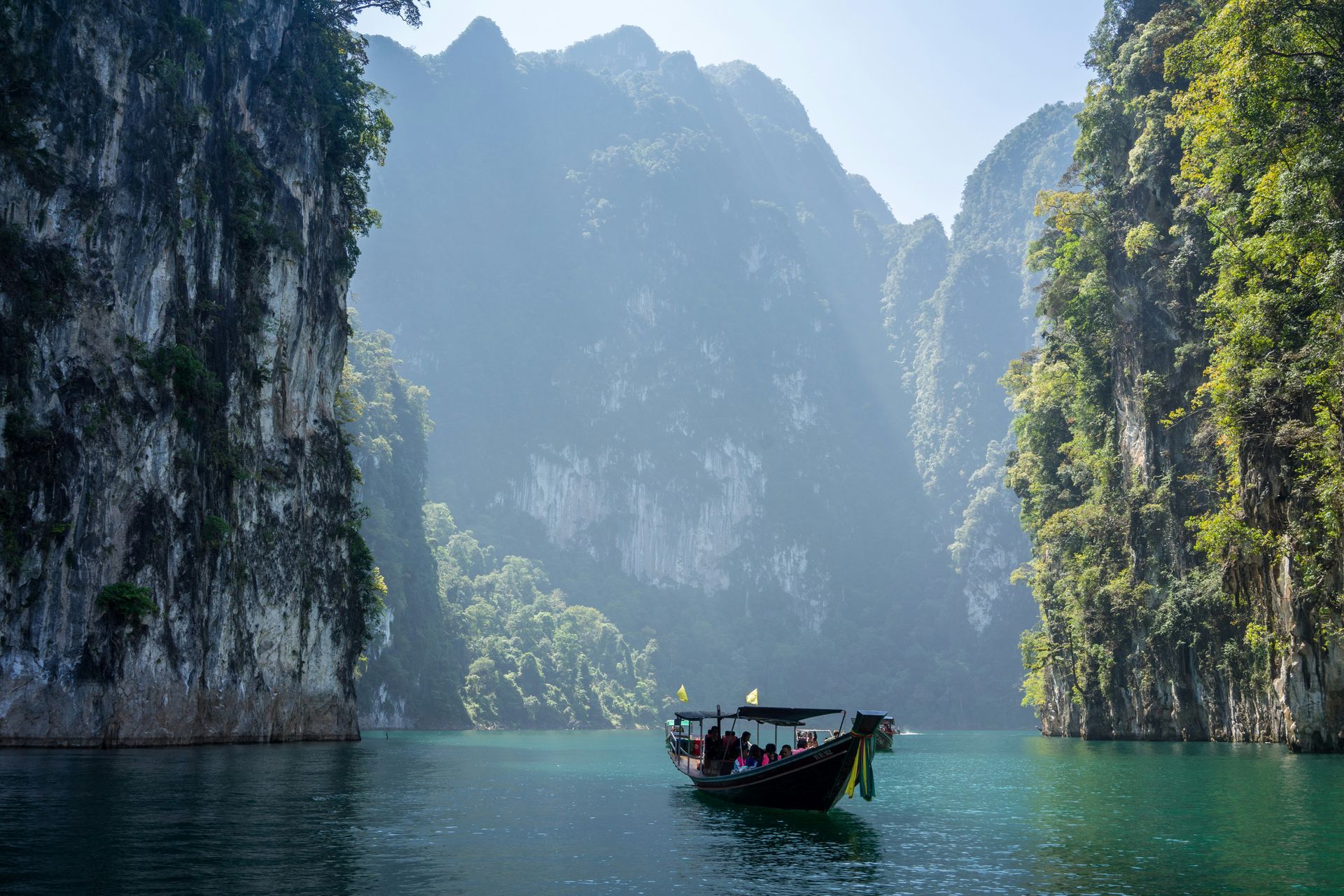 Boat on turquoise water between steep green limestone cliffs under hazy mountains