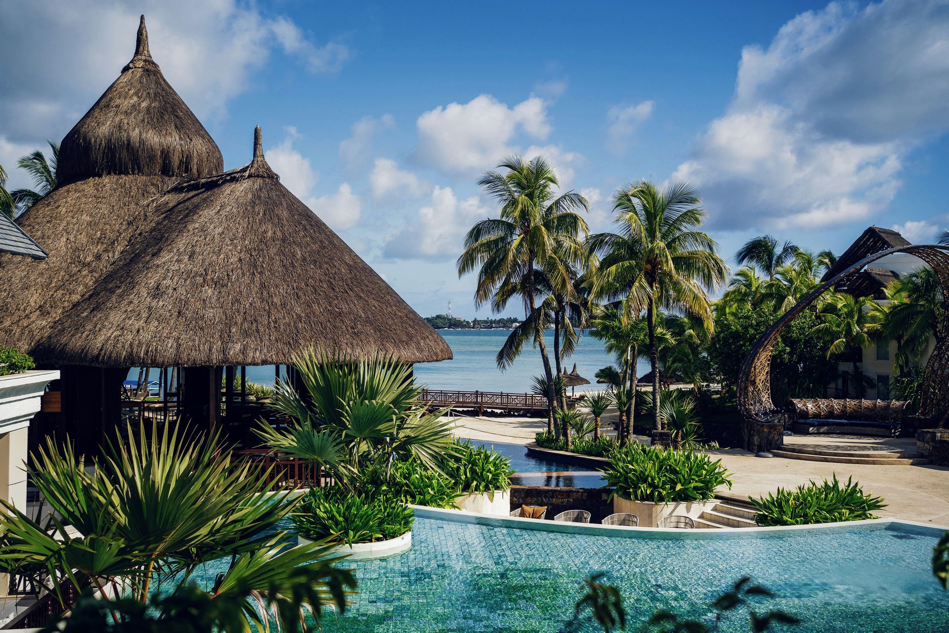 Tropical resort with thatched huts, palm trees, and a turquoise infinity pool by the sea