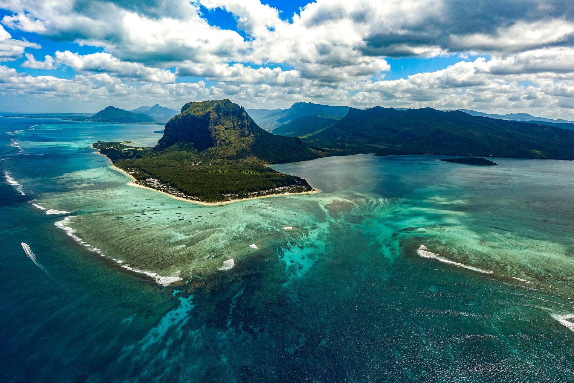 Aerial view of a tropical island with turquoise reef waters and mountains in the background
