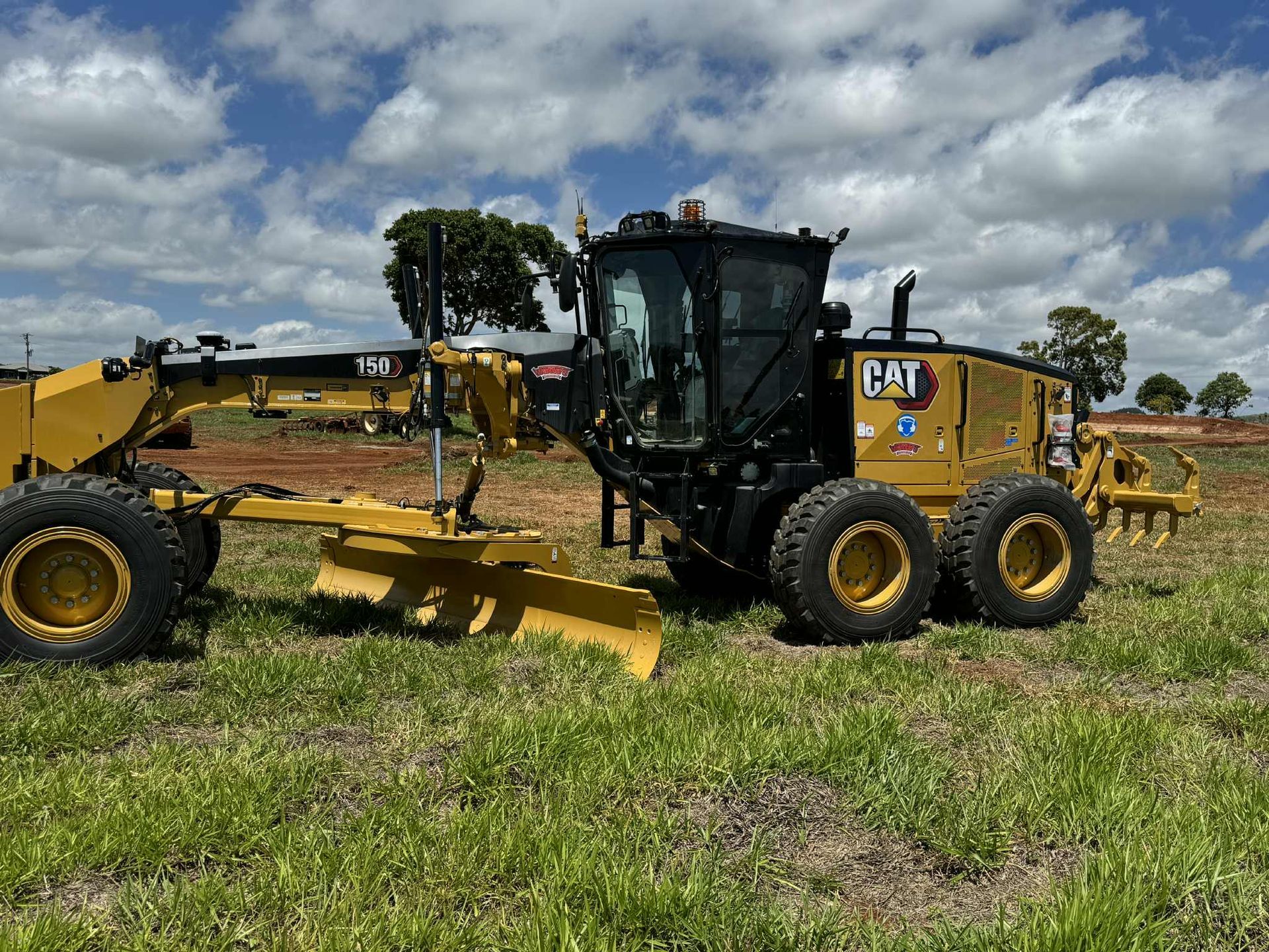 A Man Is Standing on Top of A Yellow Excavator — Watto's Earthmoving & Machinery Hire in Atherton, QLD