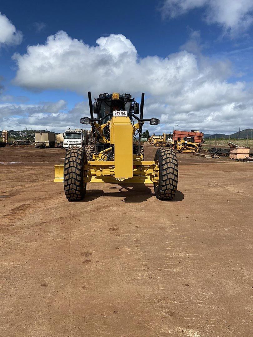 A Yellow Tractor Is Parked in A Dirt Field — Watto's Earthmoving & Machinery Hire in Atherton, QLD