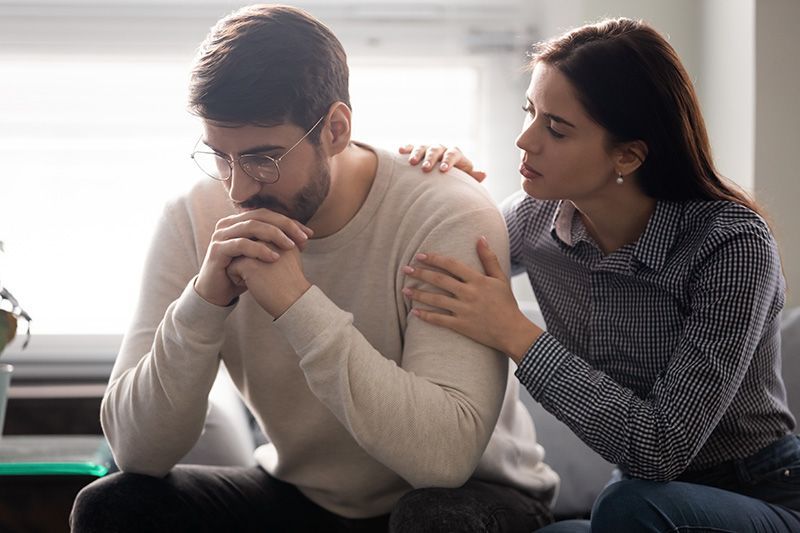 a woman is comforting a man who is sitting on a couch