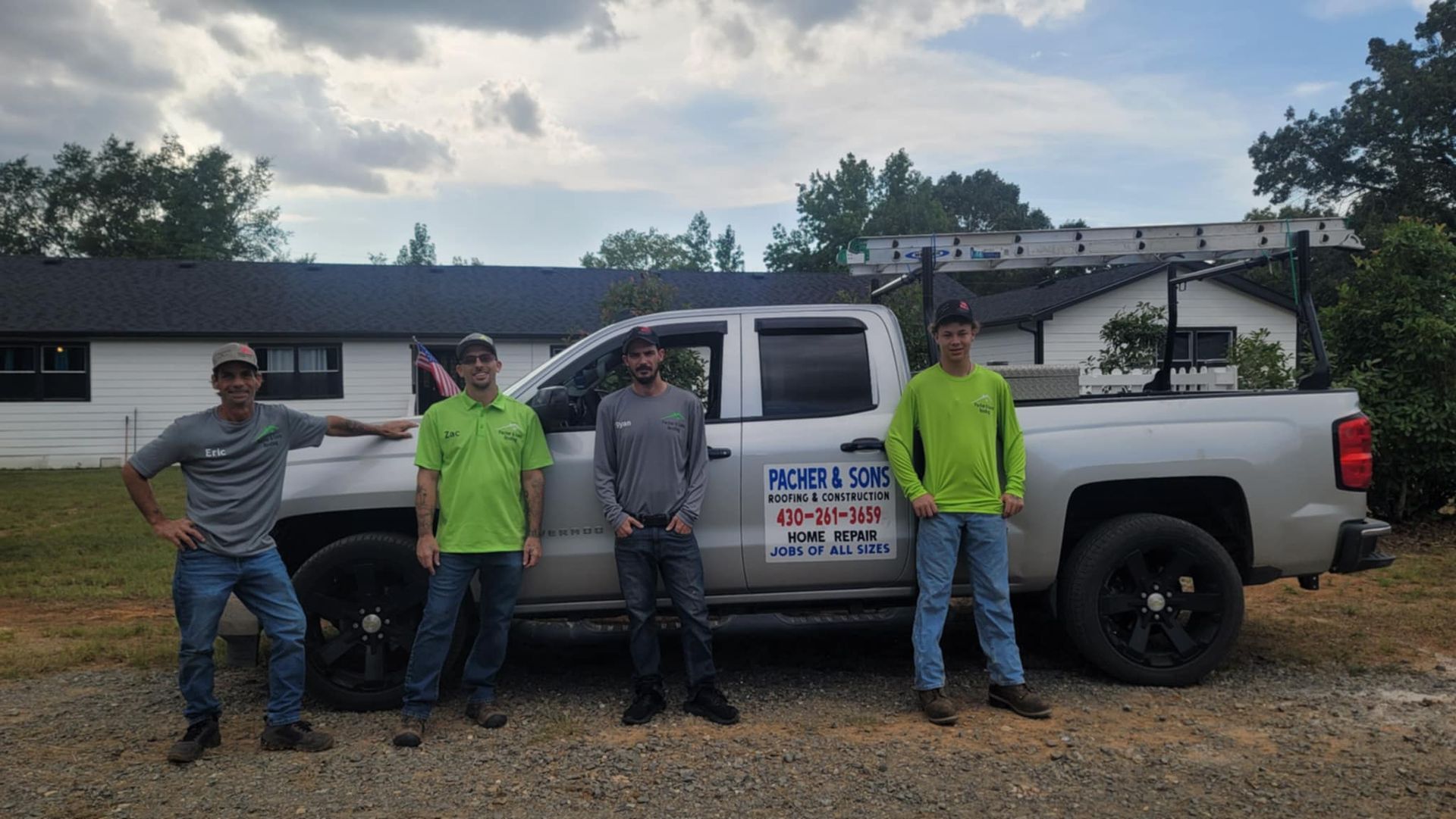 Four workers stand beside a white pickup truck in a yard, wearing neon safety shirts.