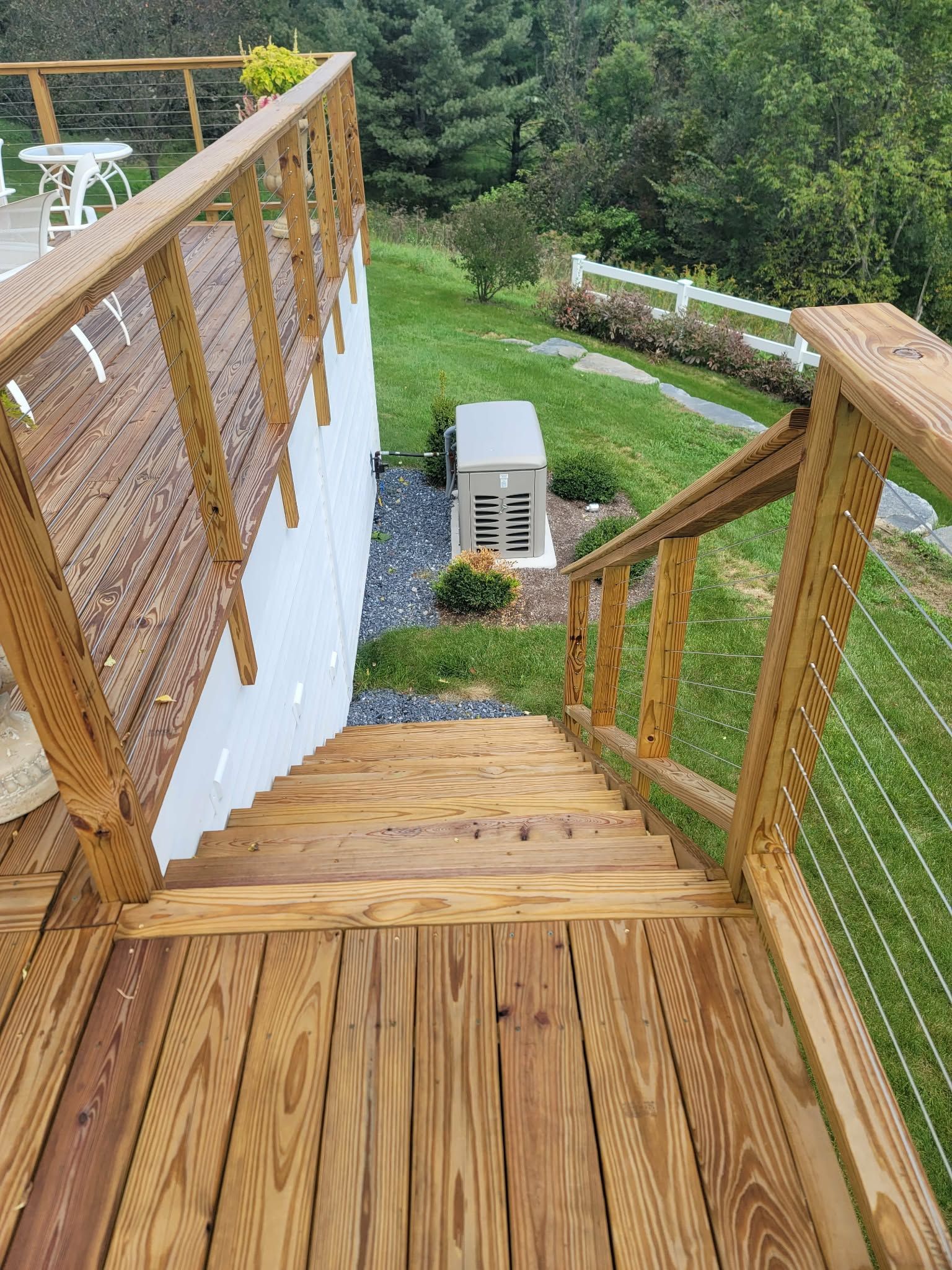Wooden outdoor staircase descending a grassy slope with railings and a wicker privacy screen