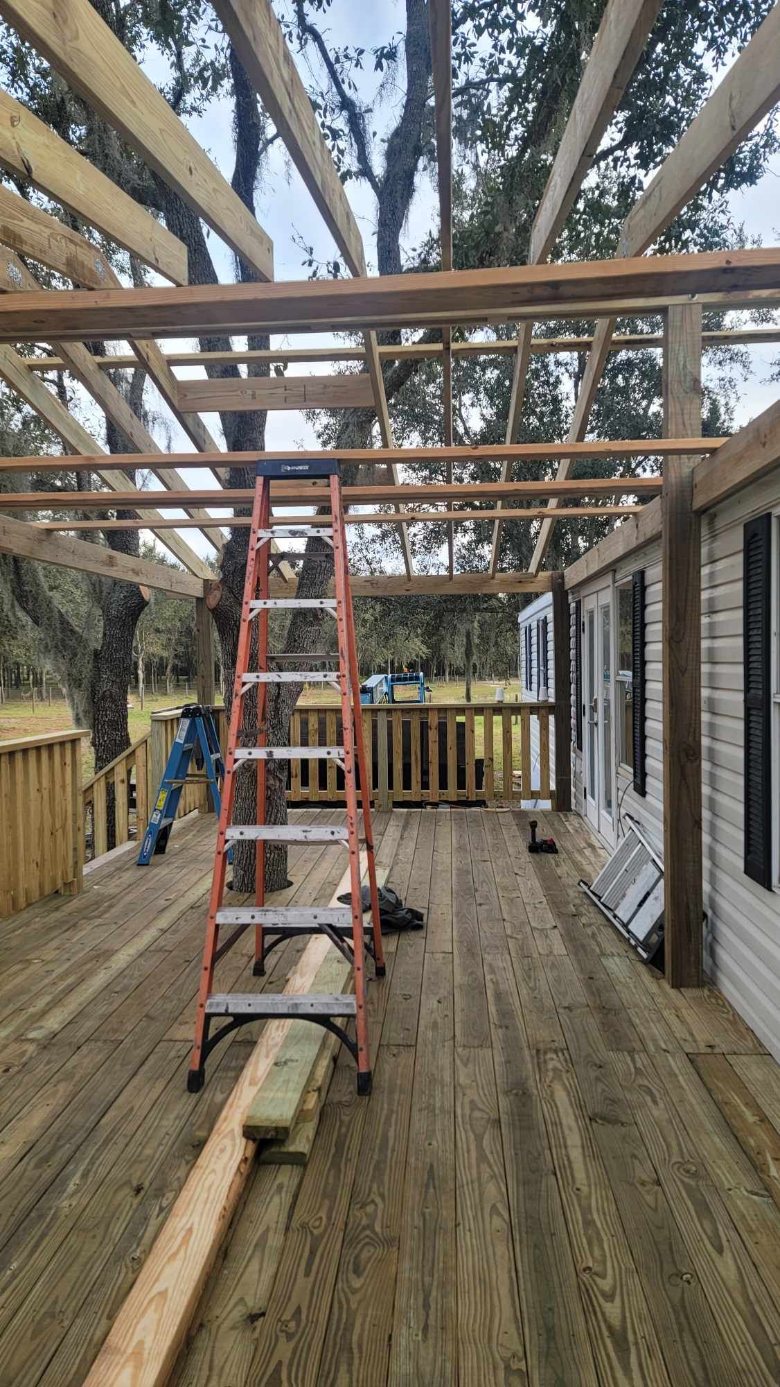 Wood deck under construction with exposed roof beams and a ladder in the center