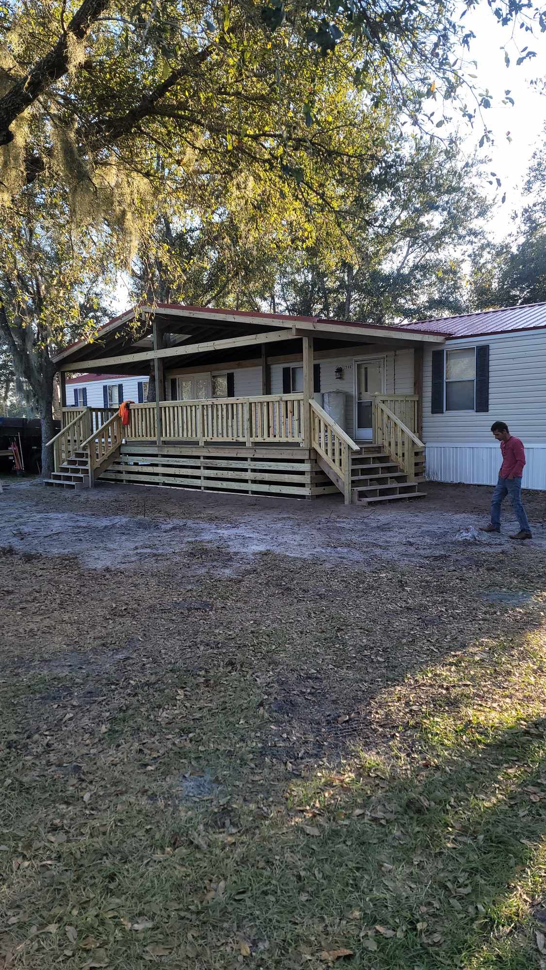 Mobile home with a new wooden porch and steps under trees, with a person standing nearby.