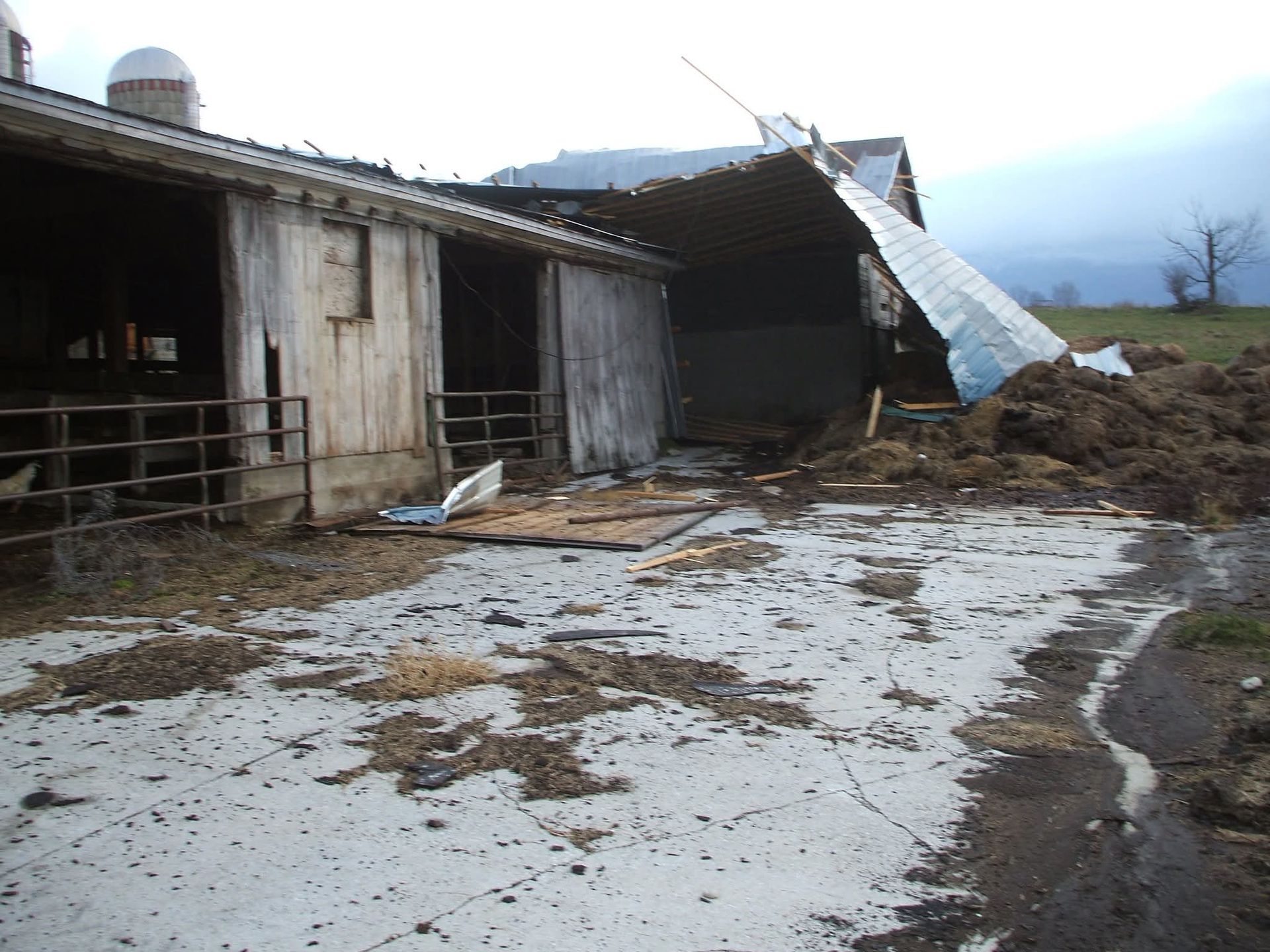 Damaged barn with collapsed roof and muddy debris after a storm or landslide