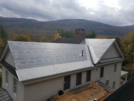 House roof covered with reflective protective sheeting, with chimney and wooded mountains in the background