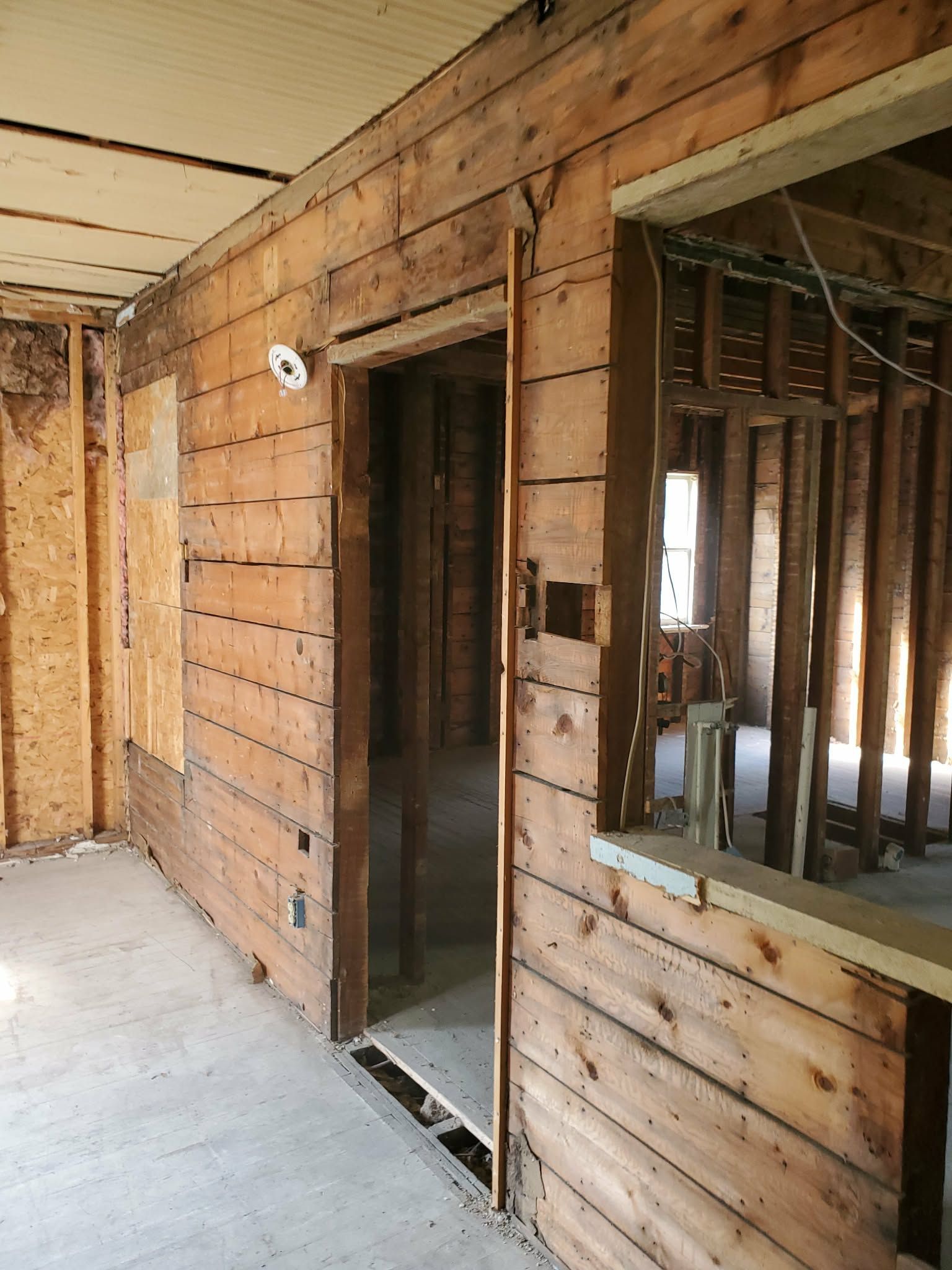 Partially renovated wooden room with exposed studs, open doorway, and large window opening