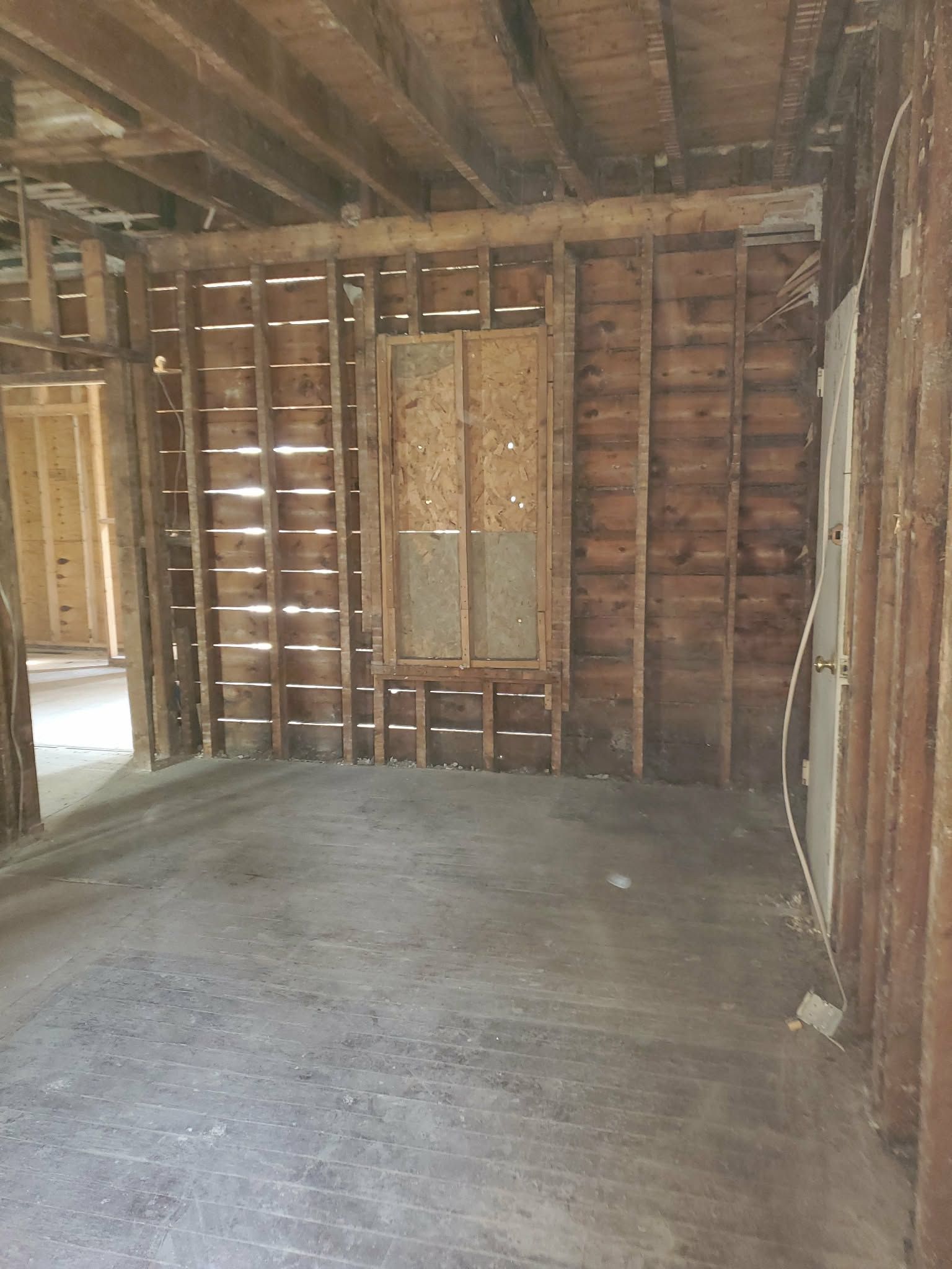 Empty unfinished room with exposed wooden studs, concrete floor, and unfinished ceiling.