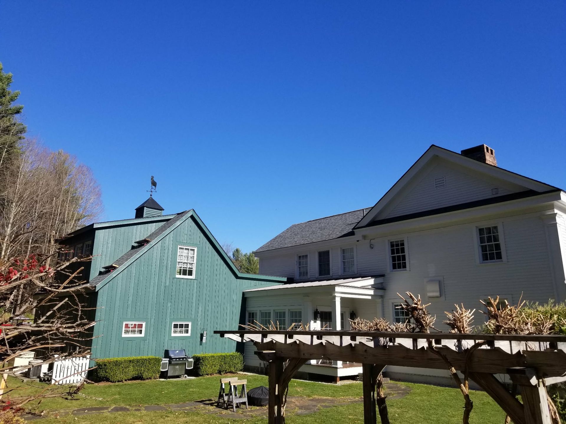 Two houses with a wooden trellis in a sunny yard under a clear blue sky