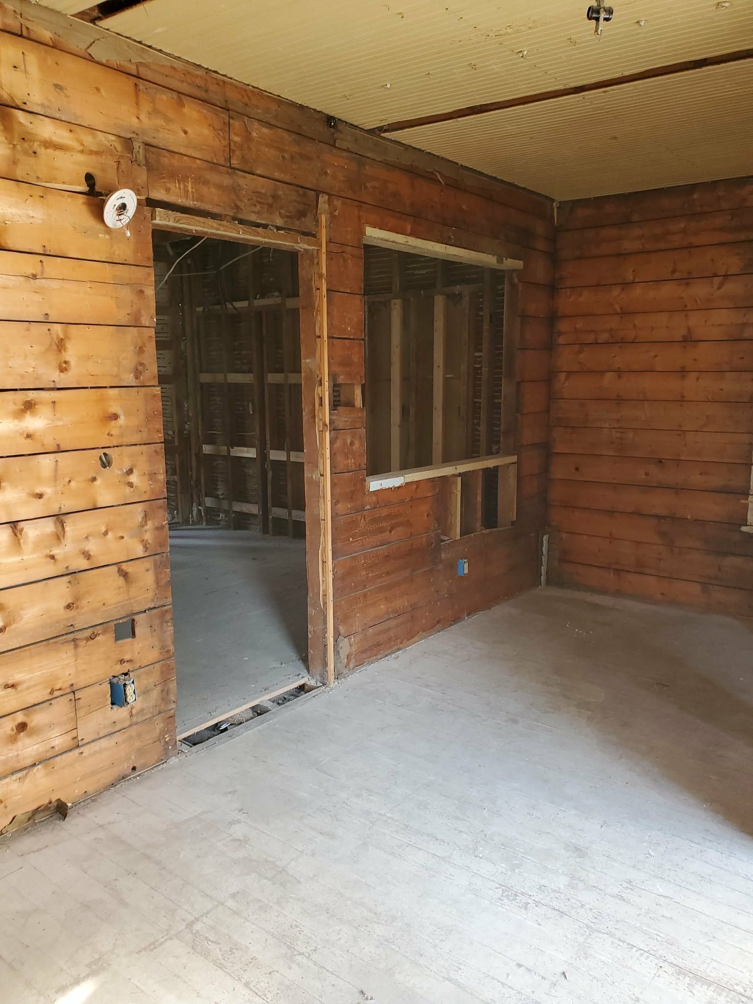 Empty unfinished room with wood-paneled walls, concrete floor, and an open doorway with windows