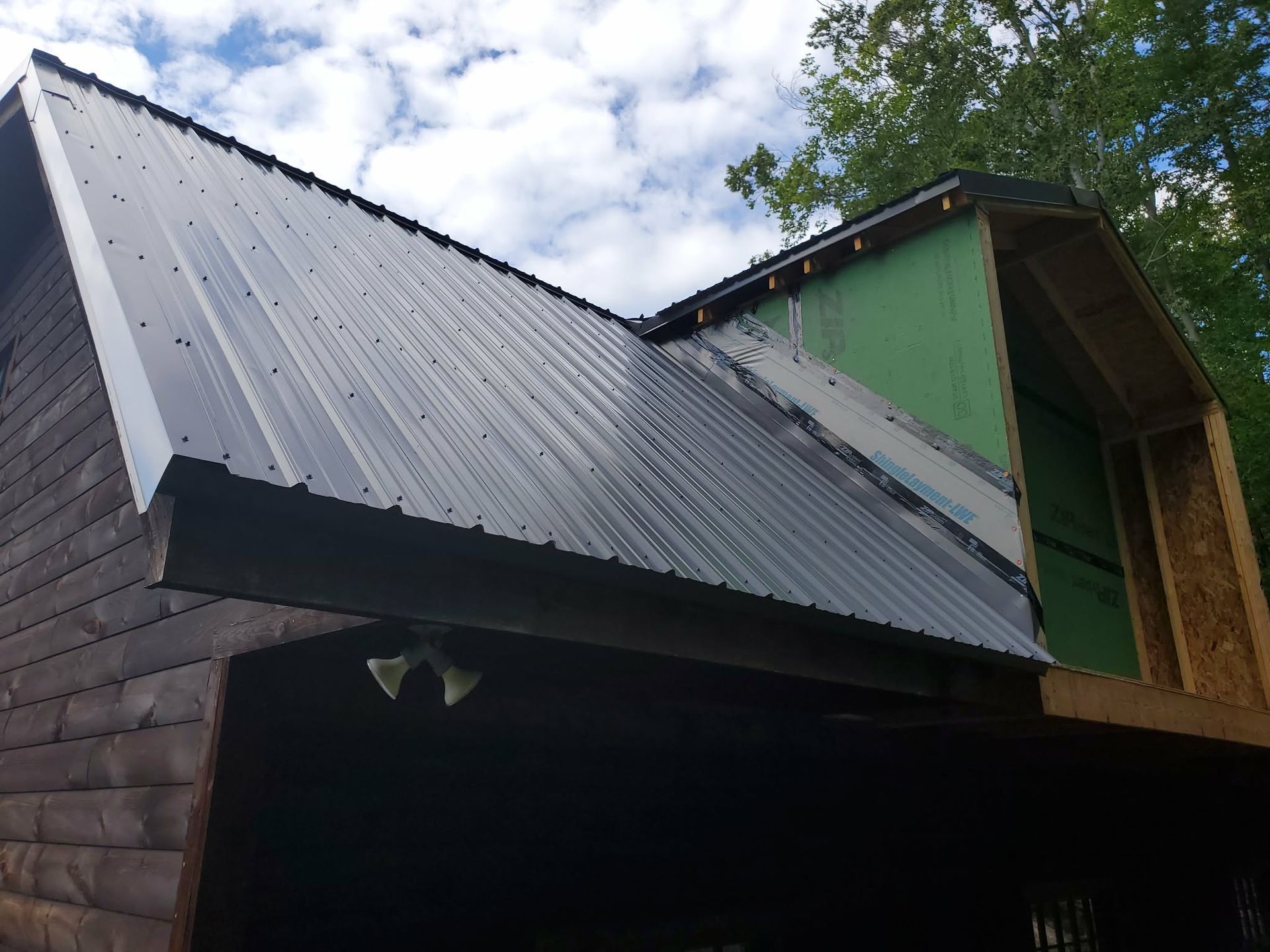 Black metal roof on a cabin with a green upper wall under a partly cloudy sky