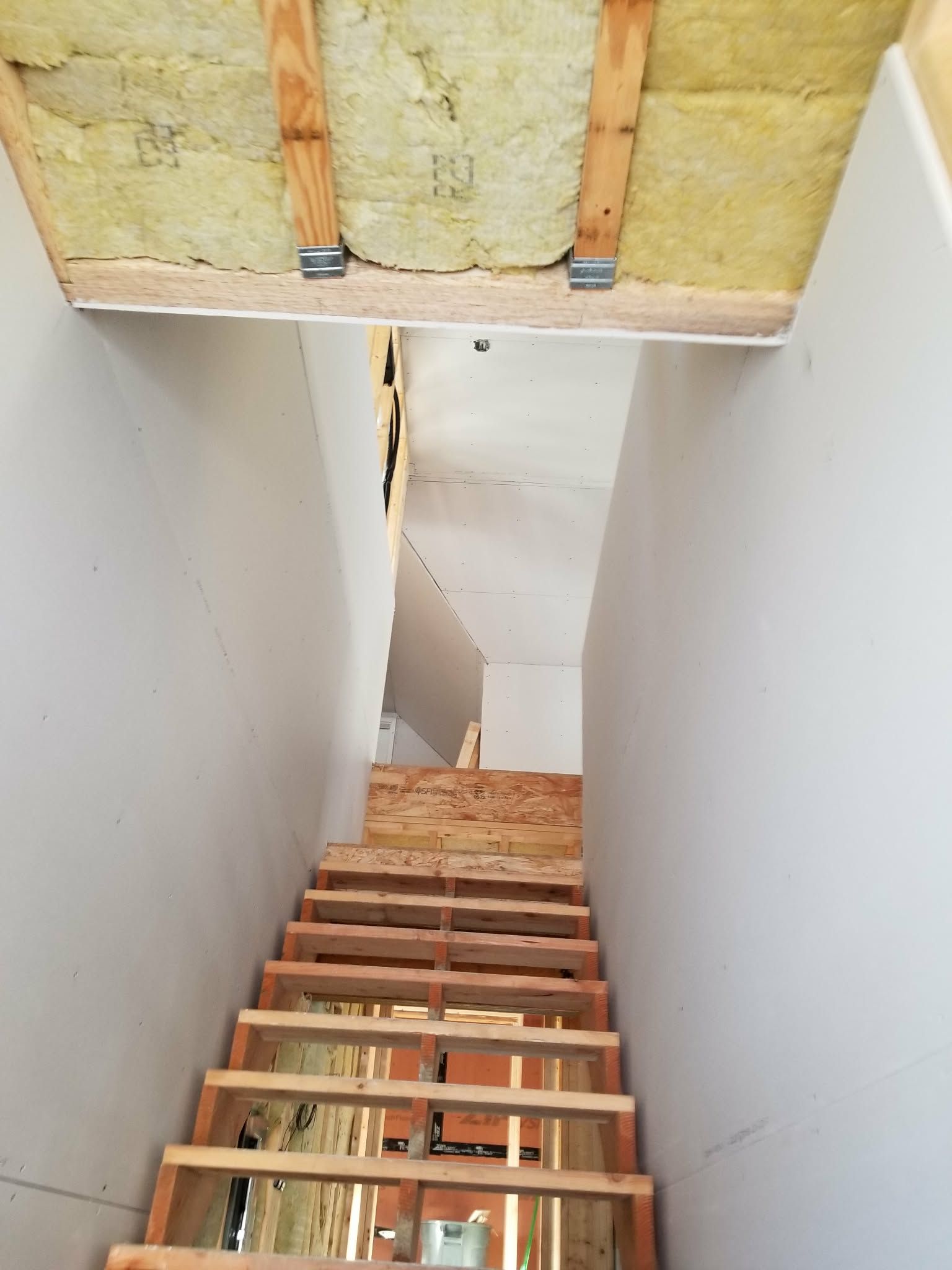 Unfinished stairwell under construction with exposed insulation and open wooden steps leading downward