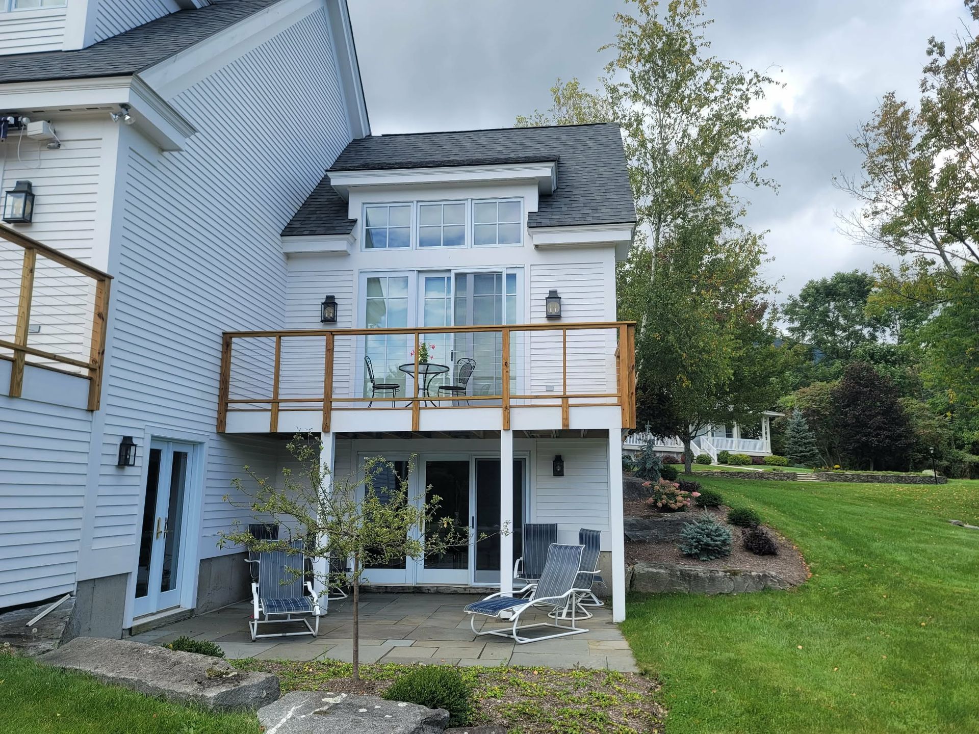 Back patio of a white house with upper deck, sliding doors, patio chairs, and a grassy yard