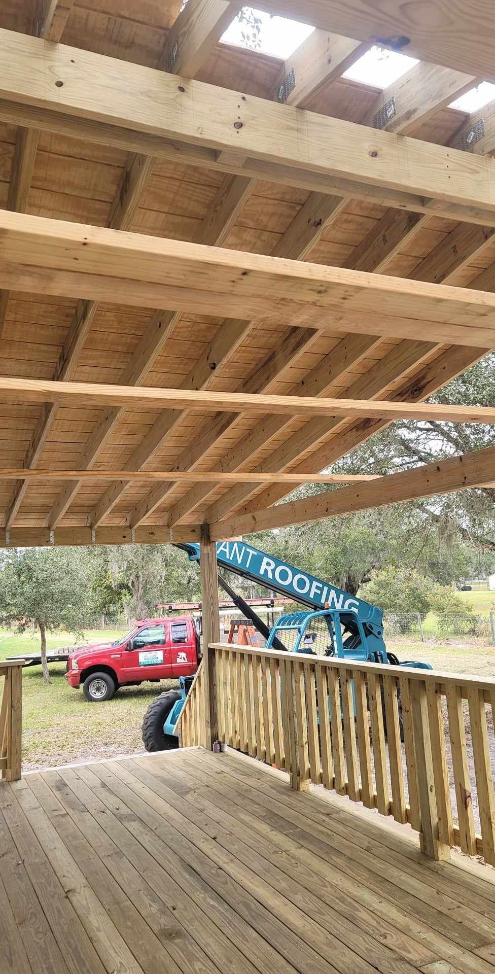 Wooden porch with a red truck and blue crane parked below, viewed from beneath a raised deck.