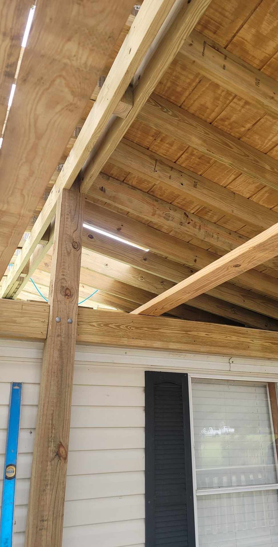 Wooden porch roof with exposed beams and a brick-and-glass wall below