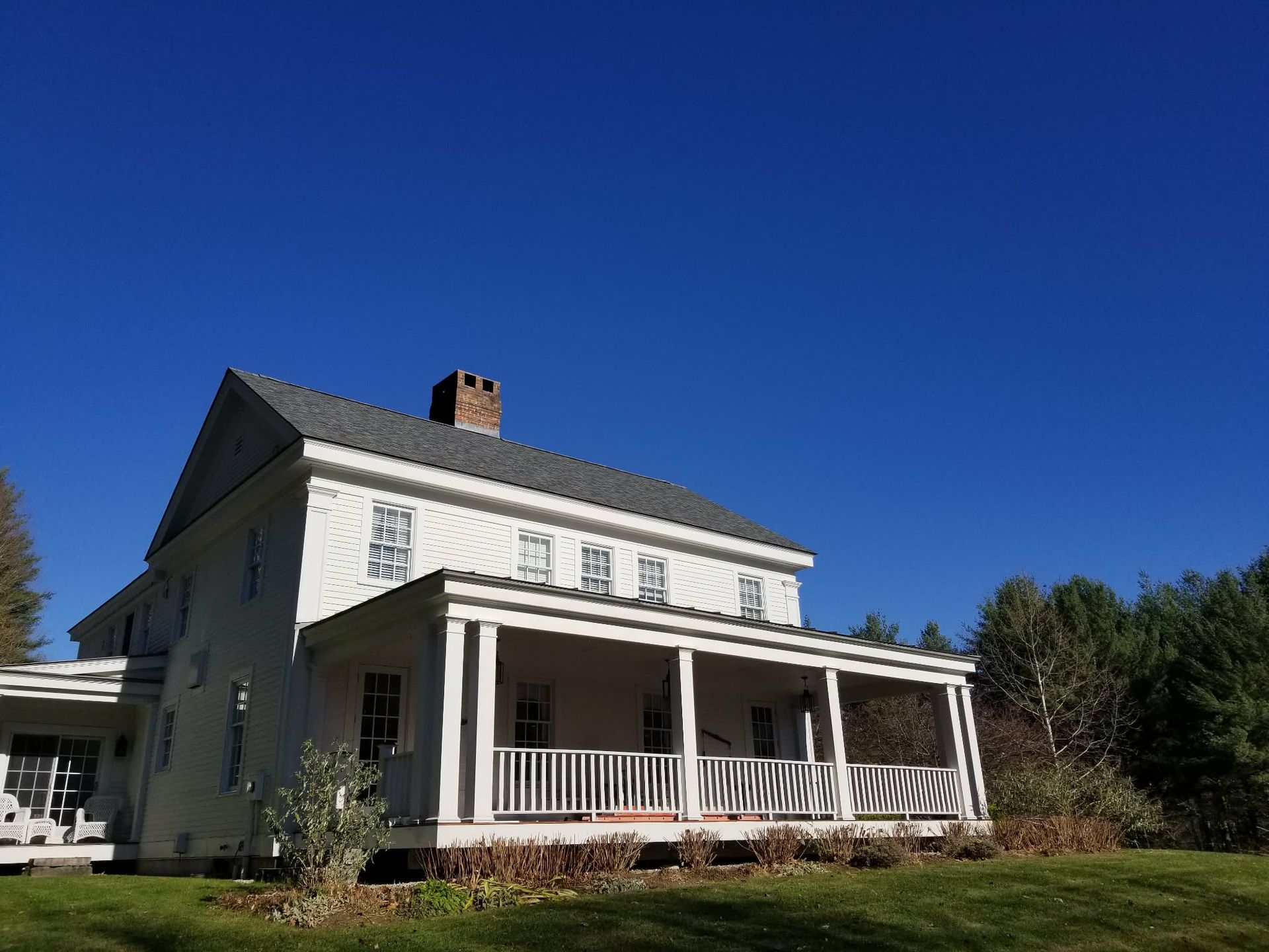 White farmhouse with wraparound porch under a clear blue sky